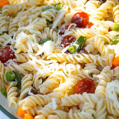 A glass bowl filled with a refreshing summer pasta salad made with rotini and fresh garden ingredients.