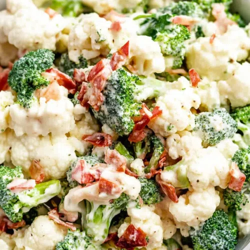 Close-up of a colorful salad with crispy vegetables, nuts, and dried fruit on a white plate.