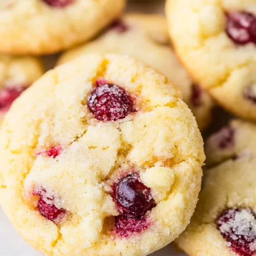 A close-up of soft, golden cookies with vibrant red cranberries on a festive background.