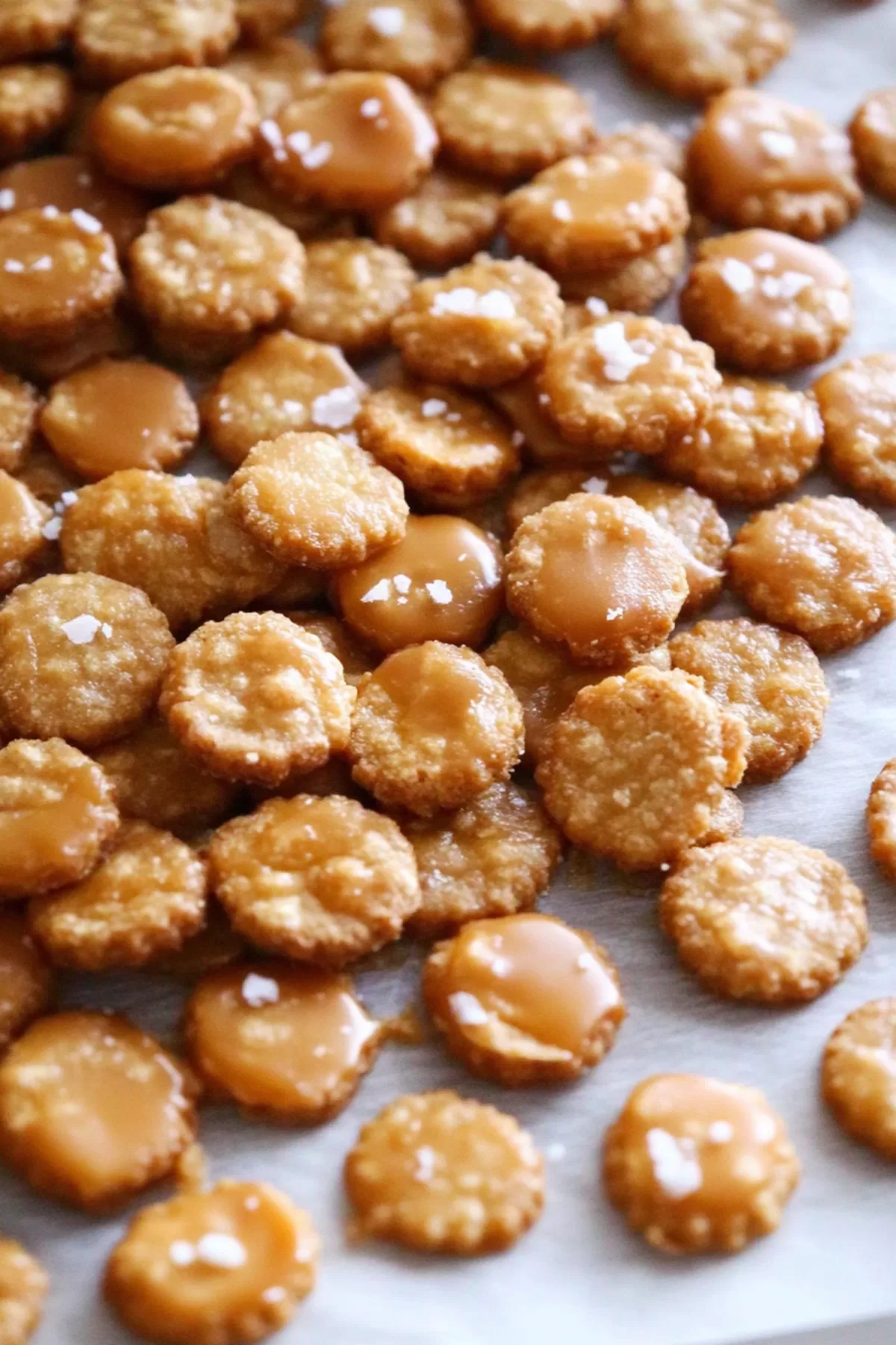 Golden crackers laid out on parchment paper, glistening with caramel and a sprinkle of salt.