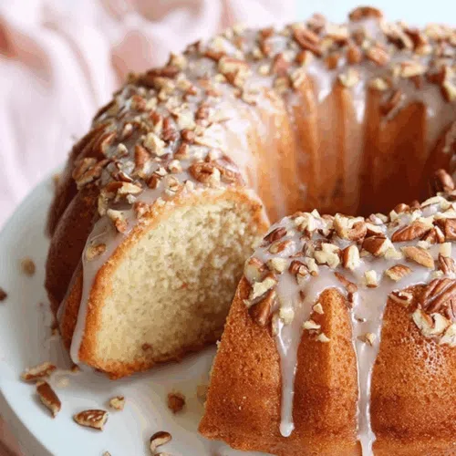 Moist golden cake slice with a glossy glaze and pecan topping on a white plate.