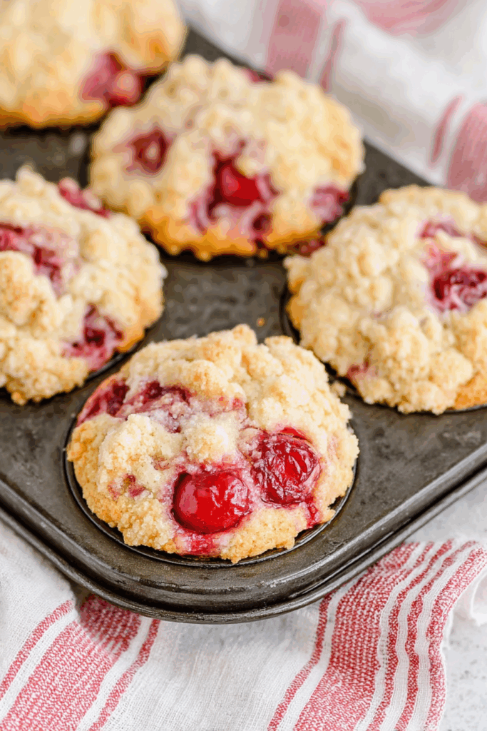 Close-up of a crumb-covered muffin with a drizzle of glaze and baked-in fruit.