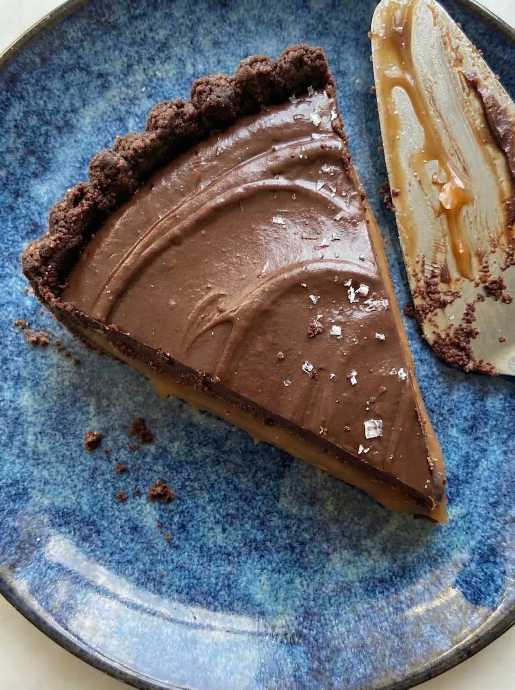 Slice of chocolate tart with thick salted caramel filling and smooth chocolate topping
