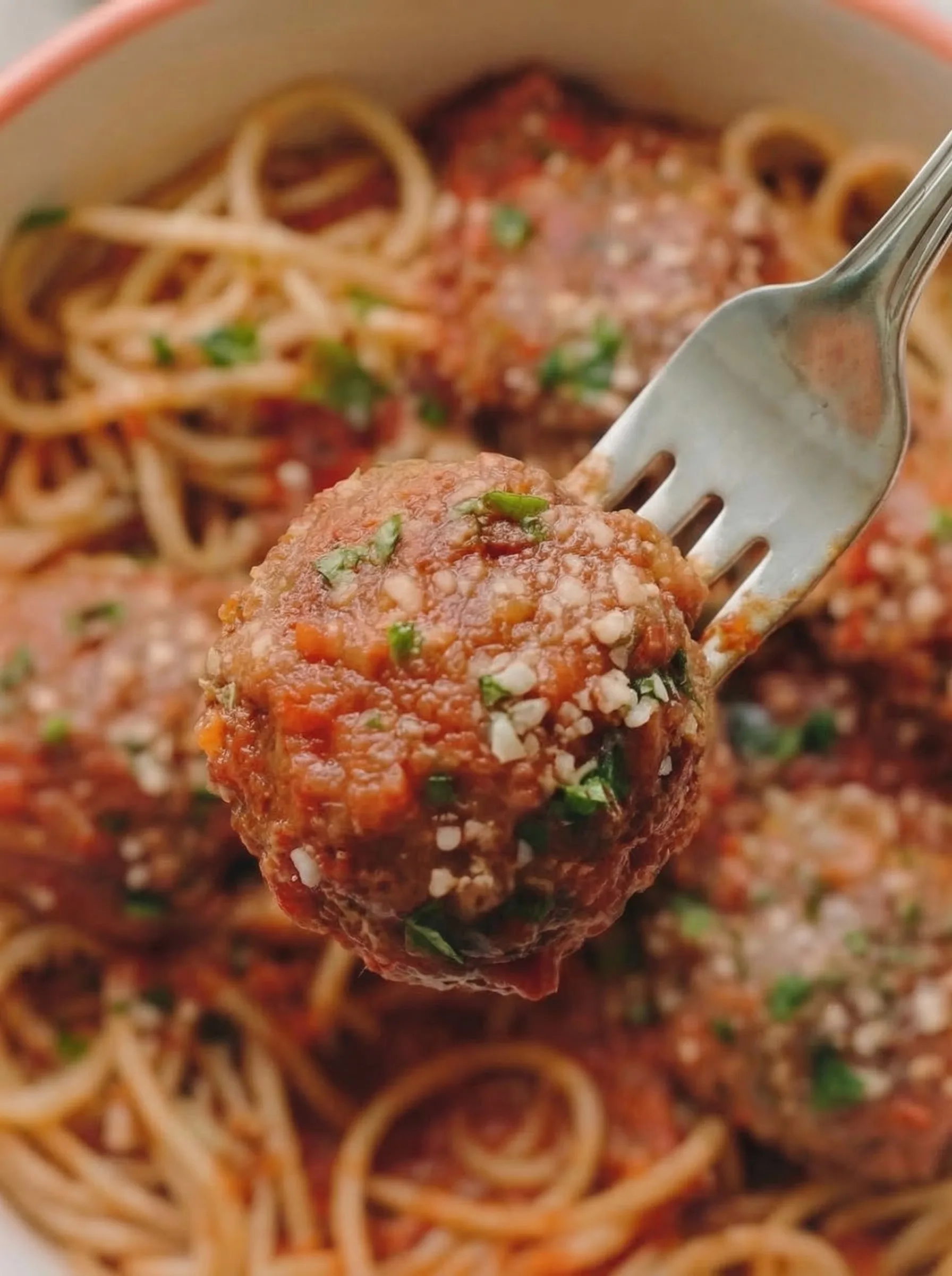 Fork lifting a Classic Italian Meatballs covered in tomato sauce and herbs