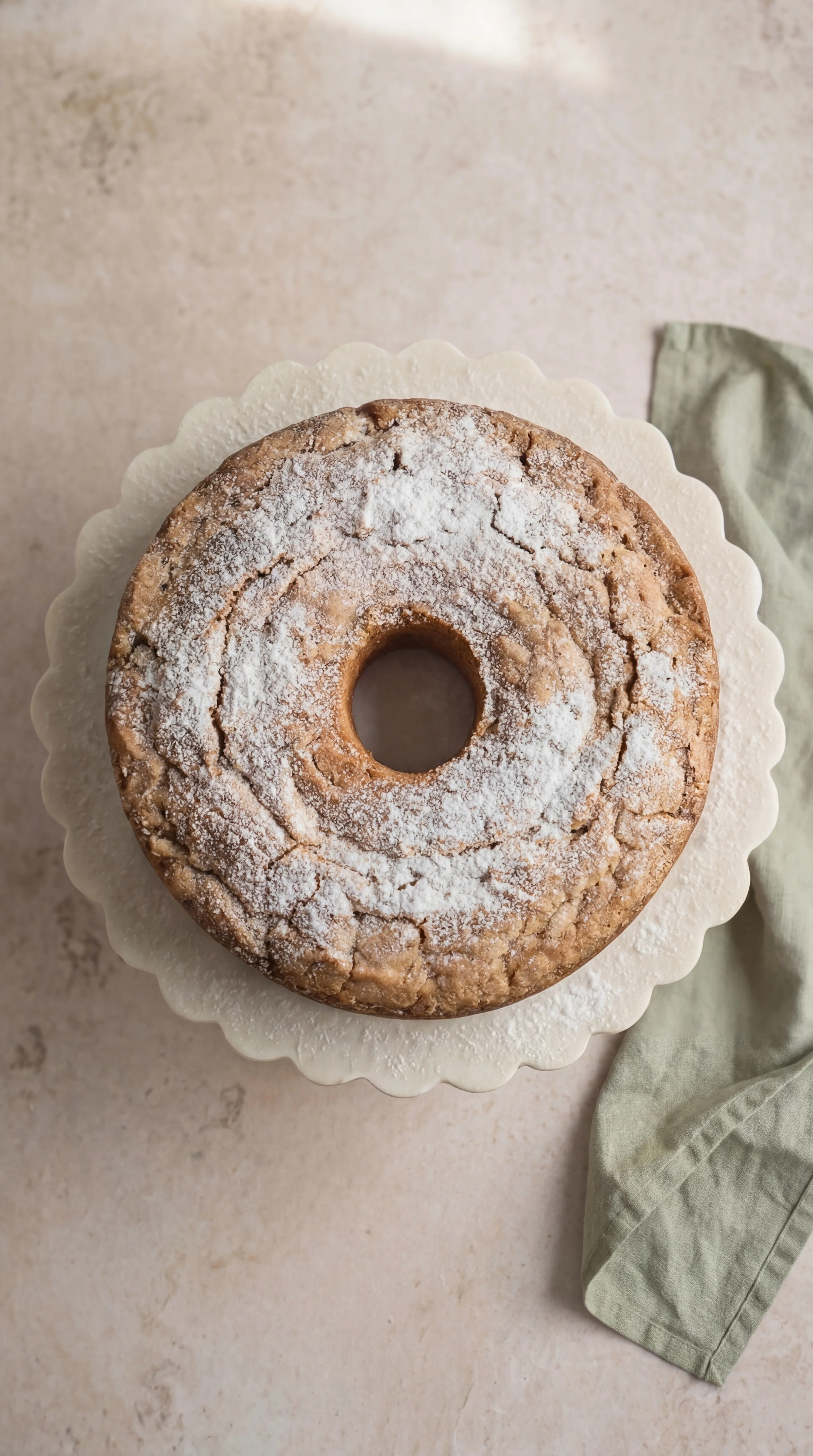 Coconut Cream Cheese Pound Cake dusted with powdered sugar on a white cake stand