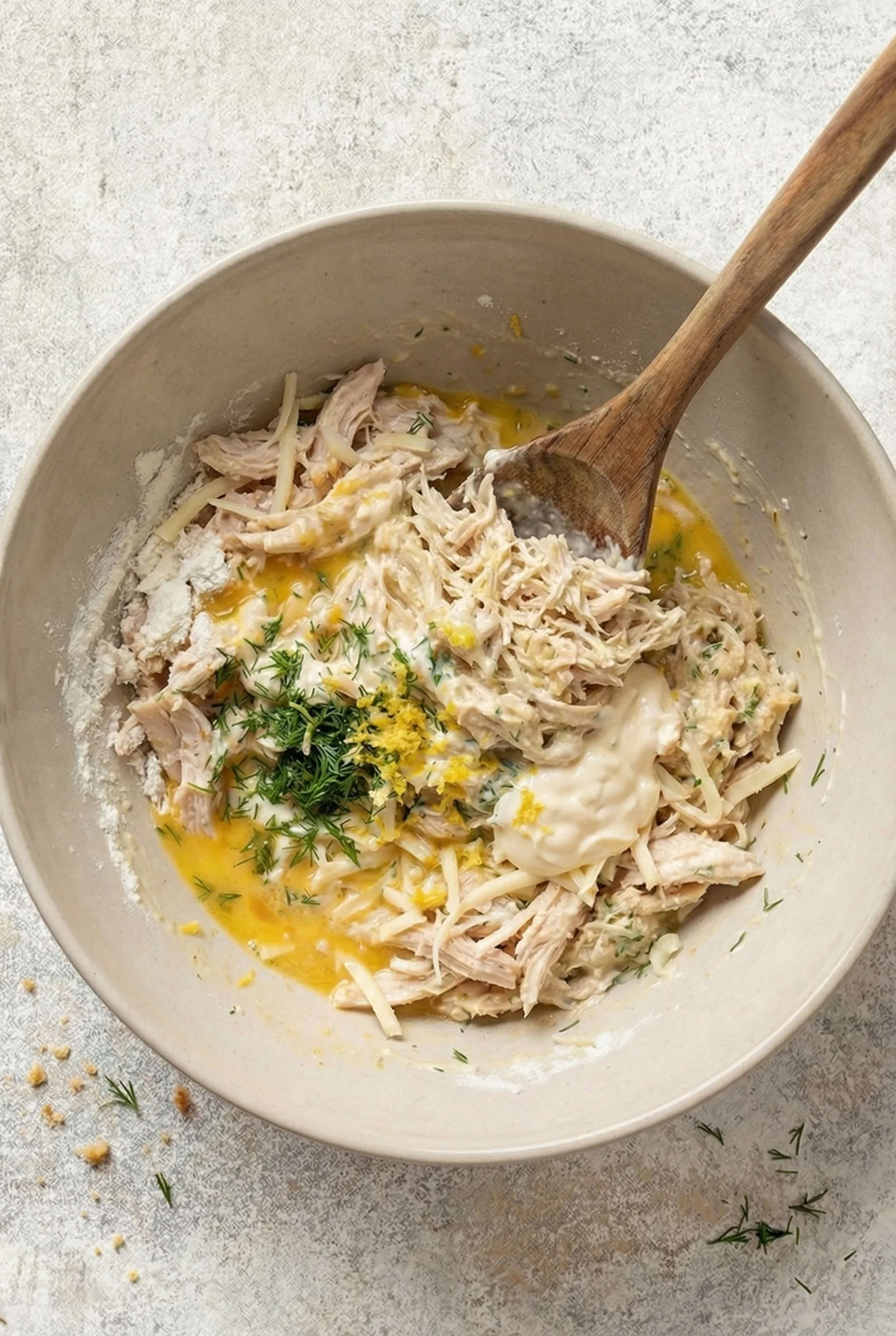mixing shredded chicken with eggs mayonnaise dill breadcrumbs and cheese in bowl for chicken patties