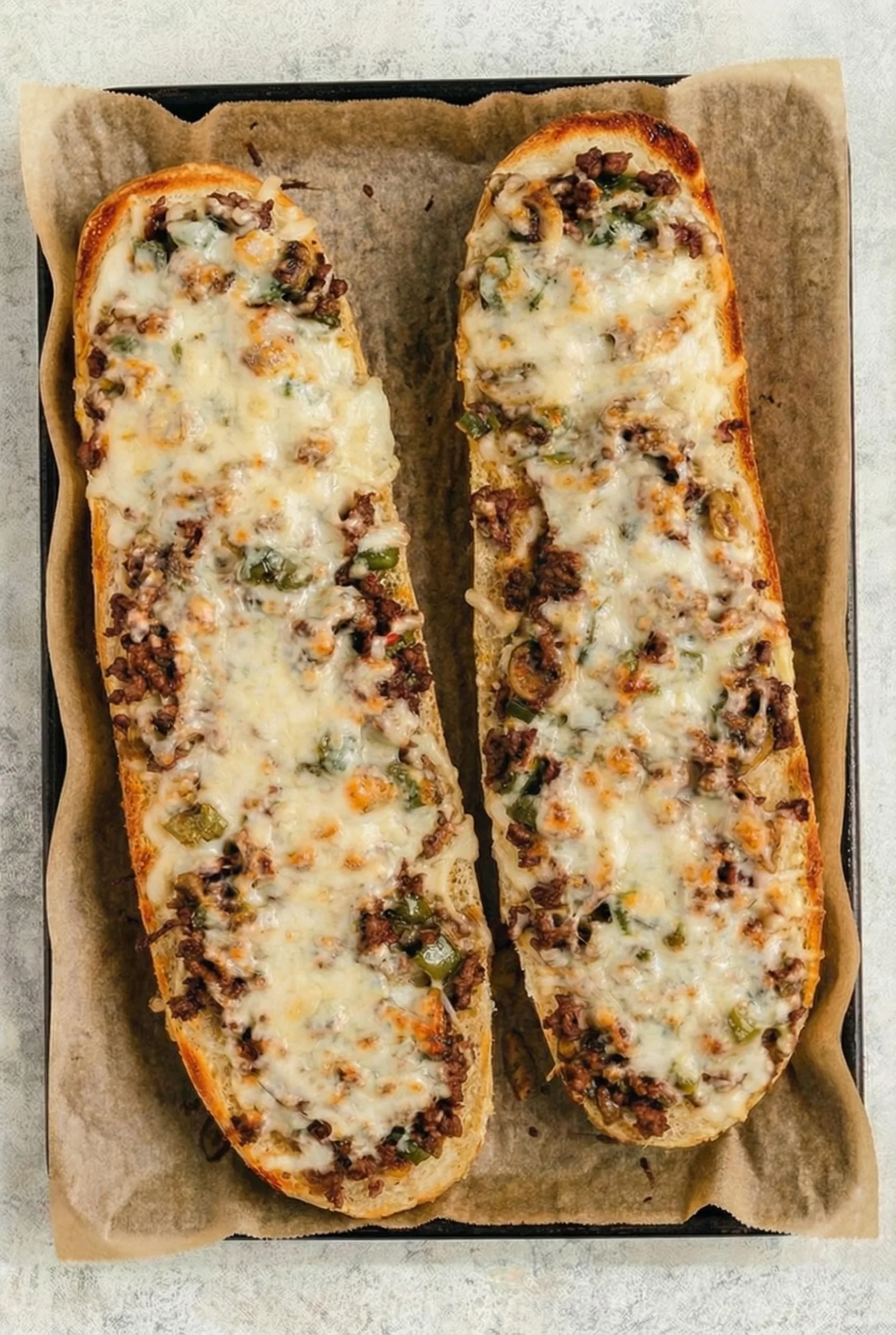 Loaded Cheesesteak Cheesy Bread topped with seasoned beef, peppers, mushrooms, and shredded cheese after baking