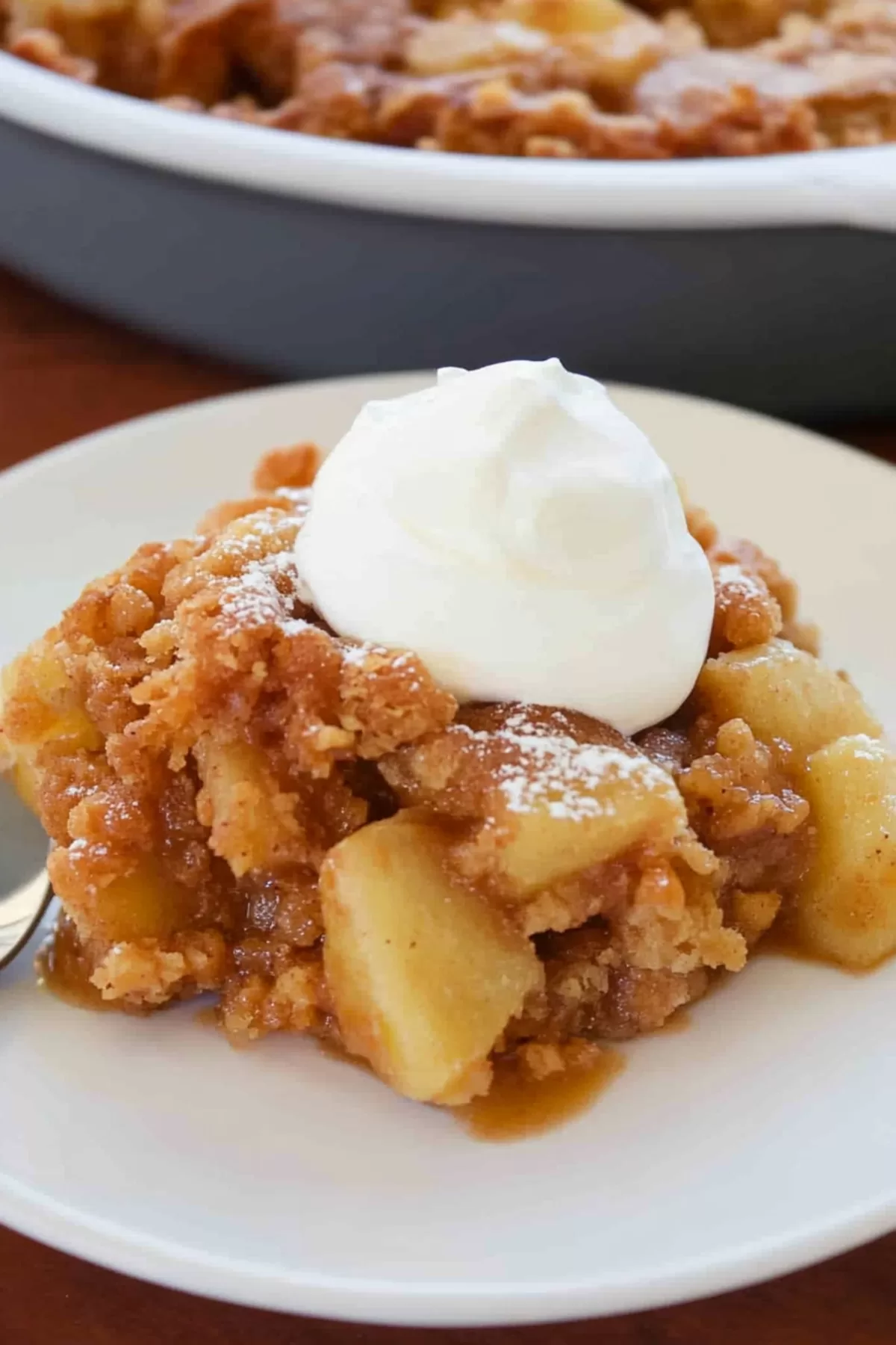 A comforting serving of Apple Brown Betty topped with whipped cream on a plate.