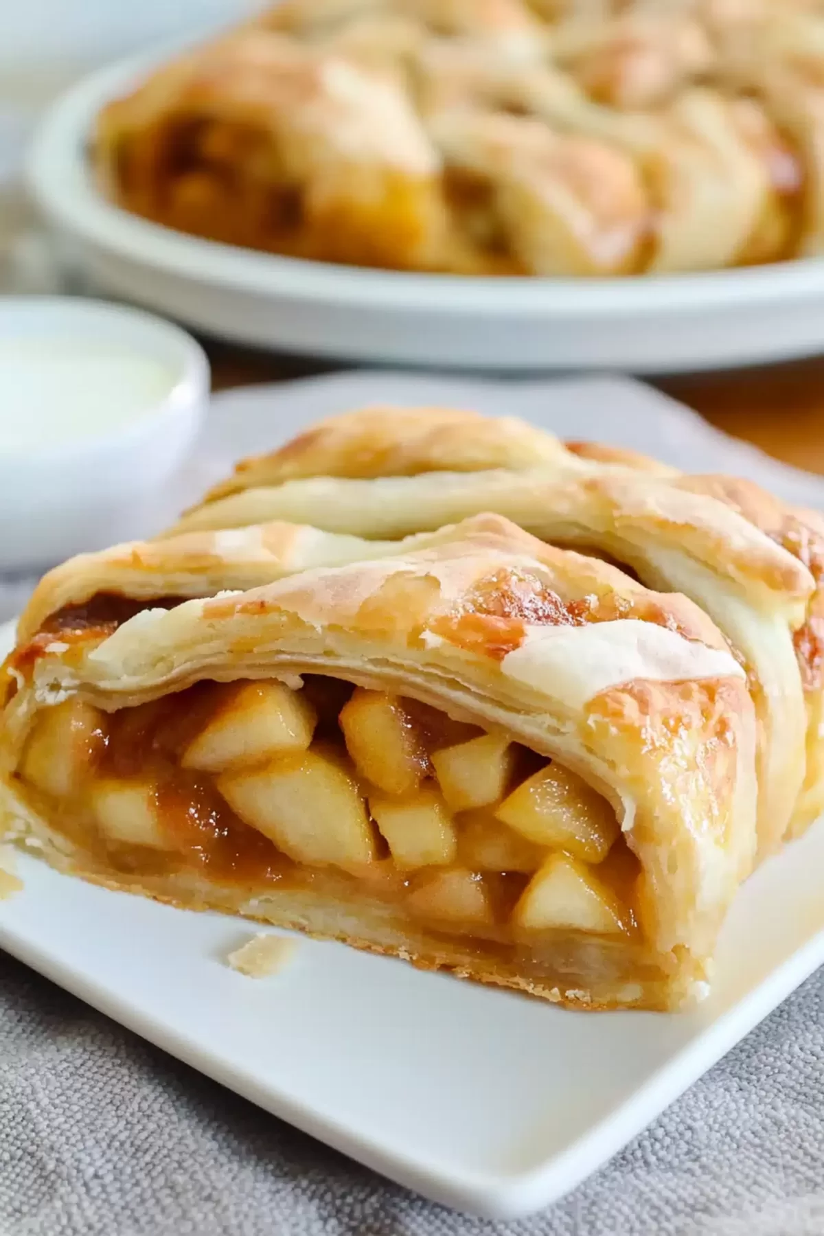 A close-up slice of apple strudel showcasing tender apple filling wrapped in flaky, golden pastry.