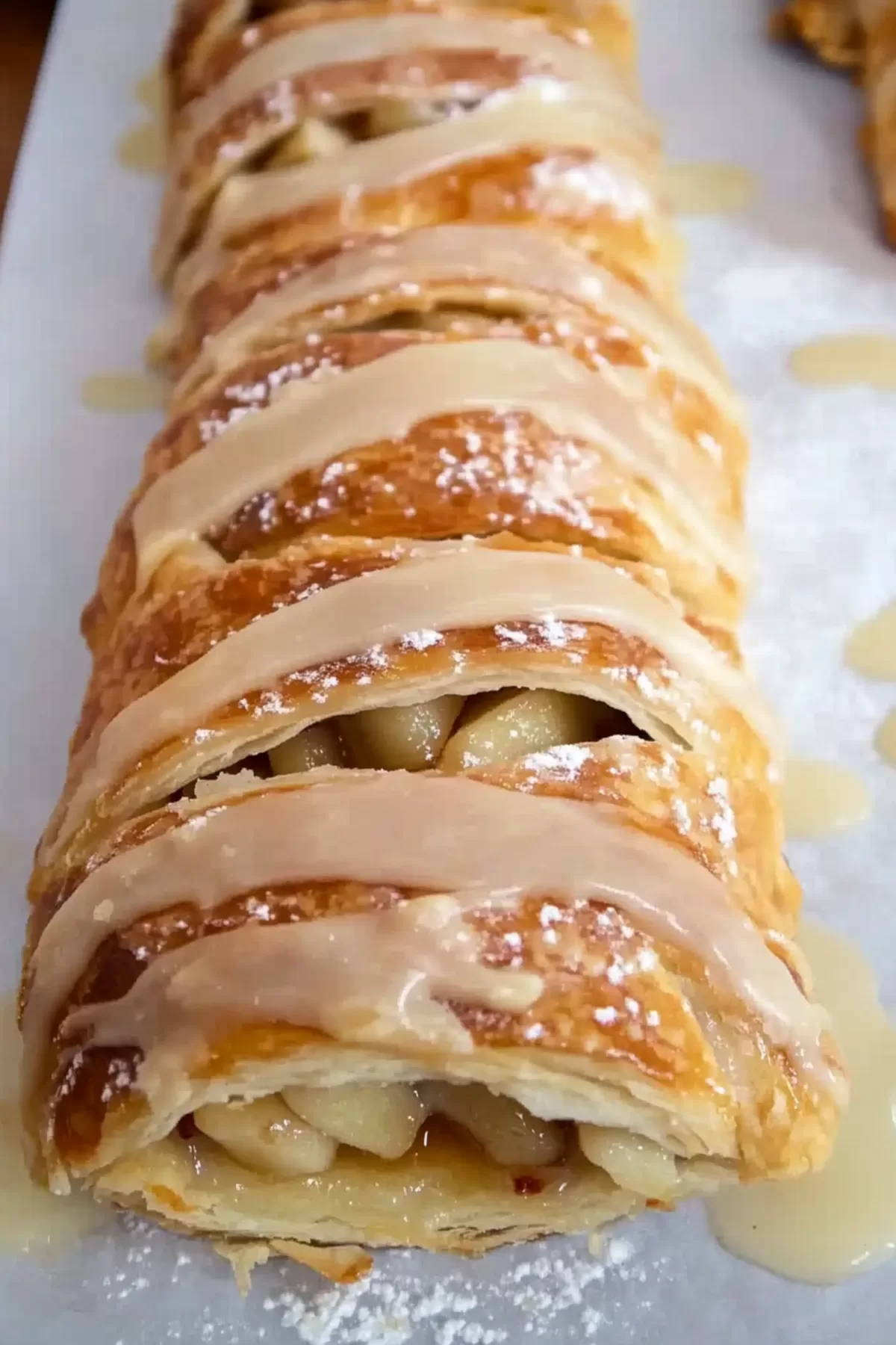 A whole apple strudel drizzled with glaze and topped with powdered sugar for a perfect finishing touch.