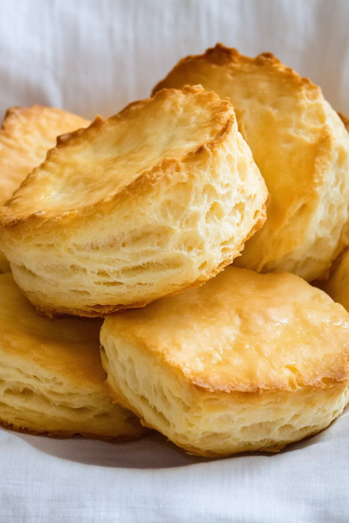 A close-up of flaky, buttery biscuits stacked on a linen napkin, highlighting their golden layers.