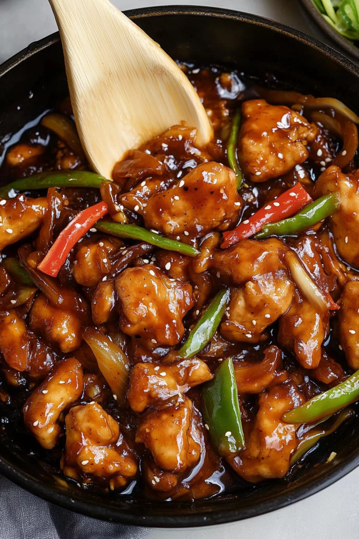 Close-up of a rich, golden-brown sauce coating bite-sized chicken and crisp vegetables.