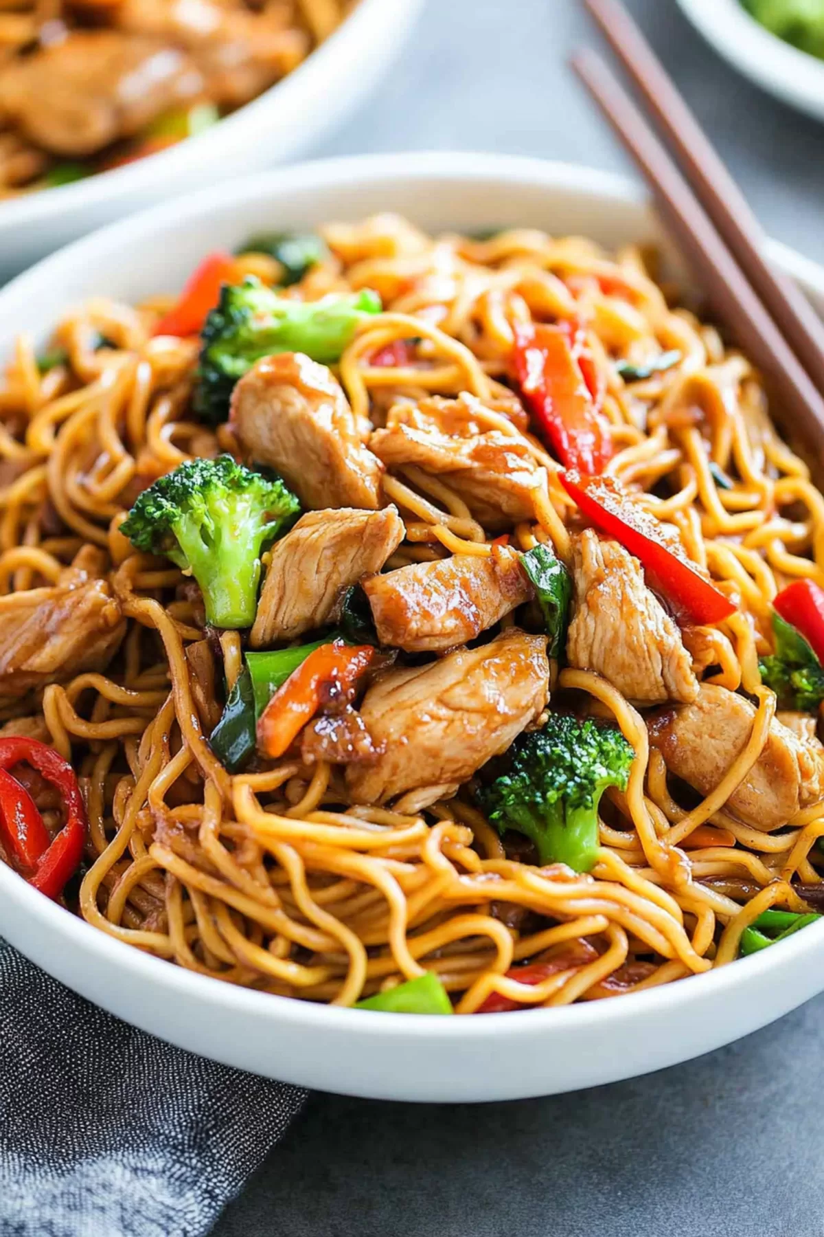 A steaming bowl of tender chicken pieces paired with springy noodles and fresh vegetables.