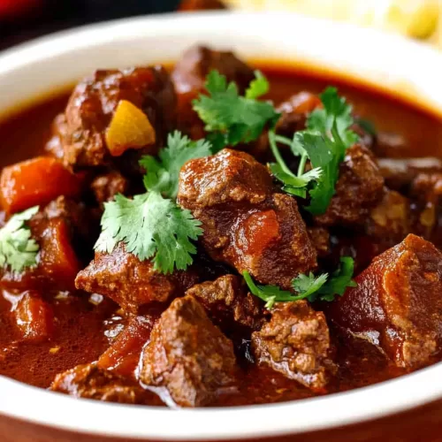 Bowl of hearty beef stew with rich, red sauce garnished with fresh cilantro.