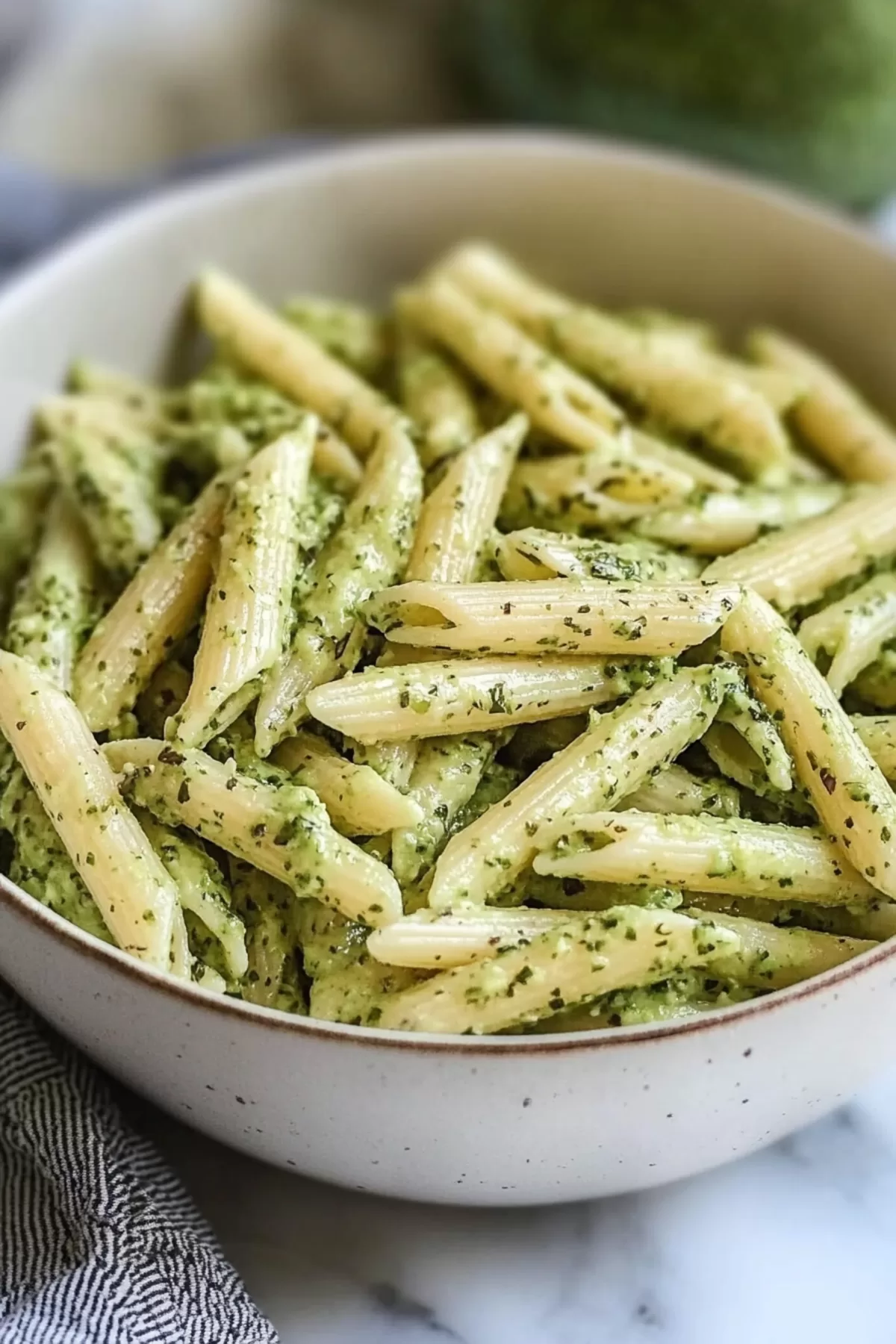 A bowl of avocado-infused pasta with a drizzle of olive oil and fresh basil leaves on top.