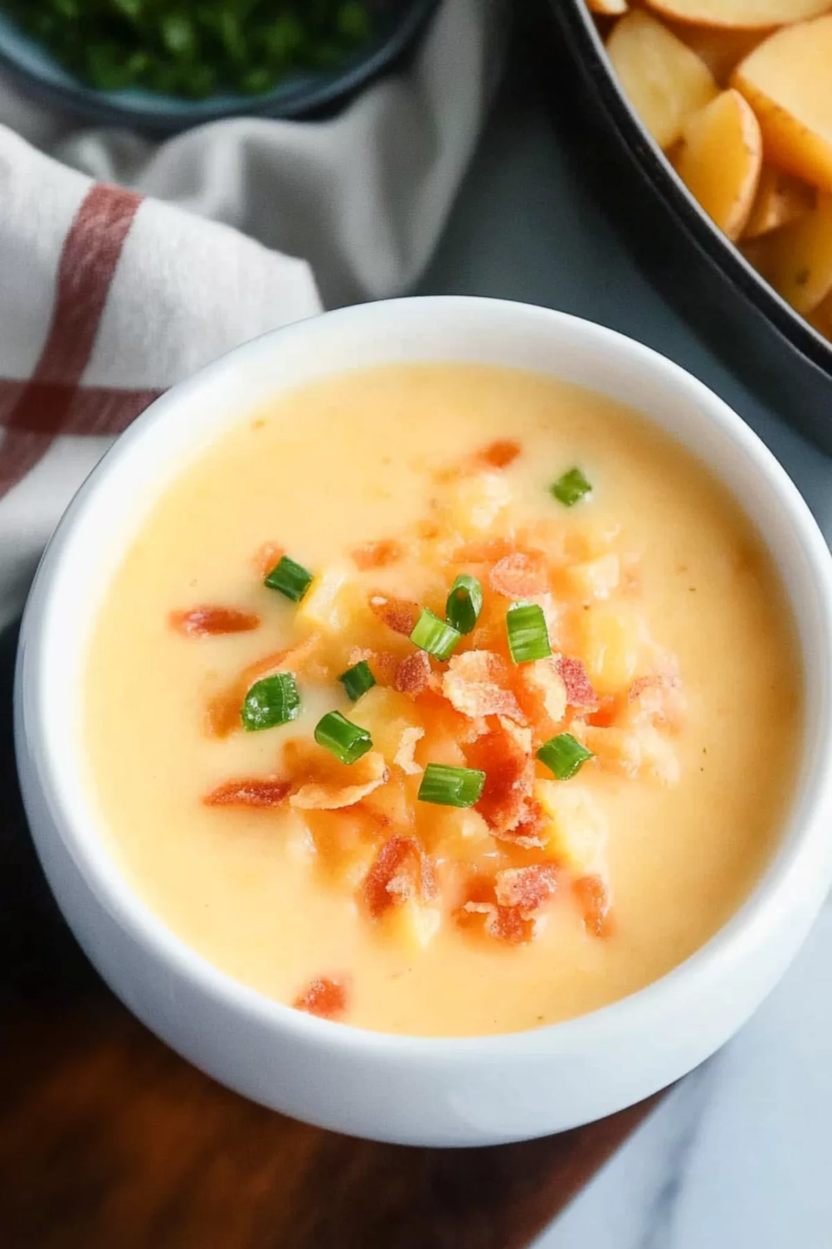 Close-up of a hearty, cheesy soup with vibrant toppings served in a clean white bowl on a wooden surface.