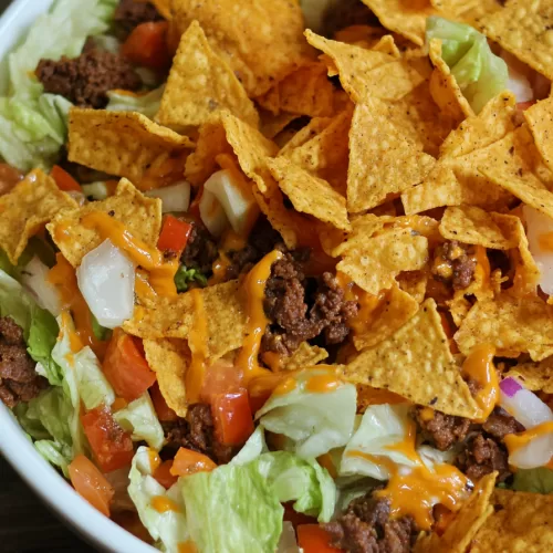 Close-up of a colorful taco salad loaded with toppings and crispy ingredients.