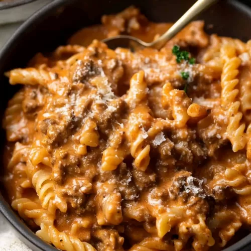 Individual serving of pasta with minced meat sauce, topped with fresh herbs and a sprinkle of cheese for added flavor.