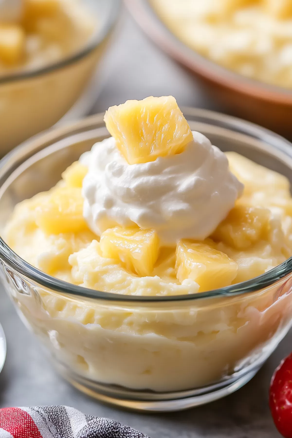 Close-up of a creamy dessert topped with fresh pineapple chunks in a glass dish.