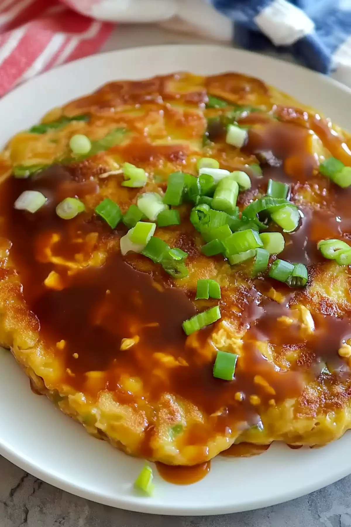 Egg Foo Young served on a white plate, glistening with a rich sauce and garnished with fresh green onions for added texture and flavor