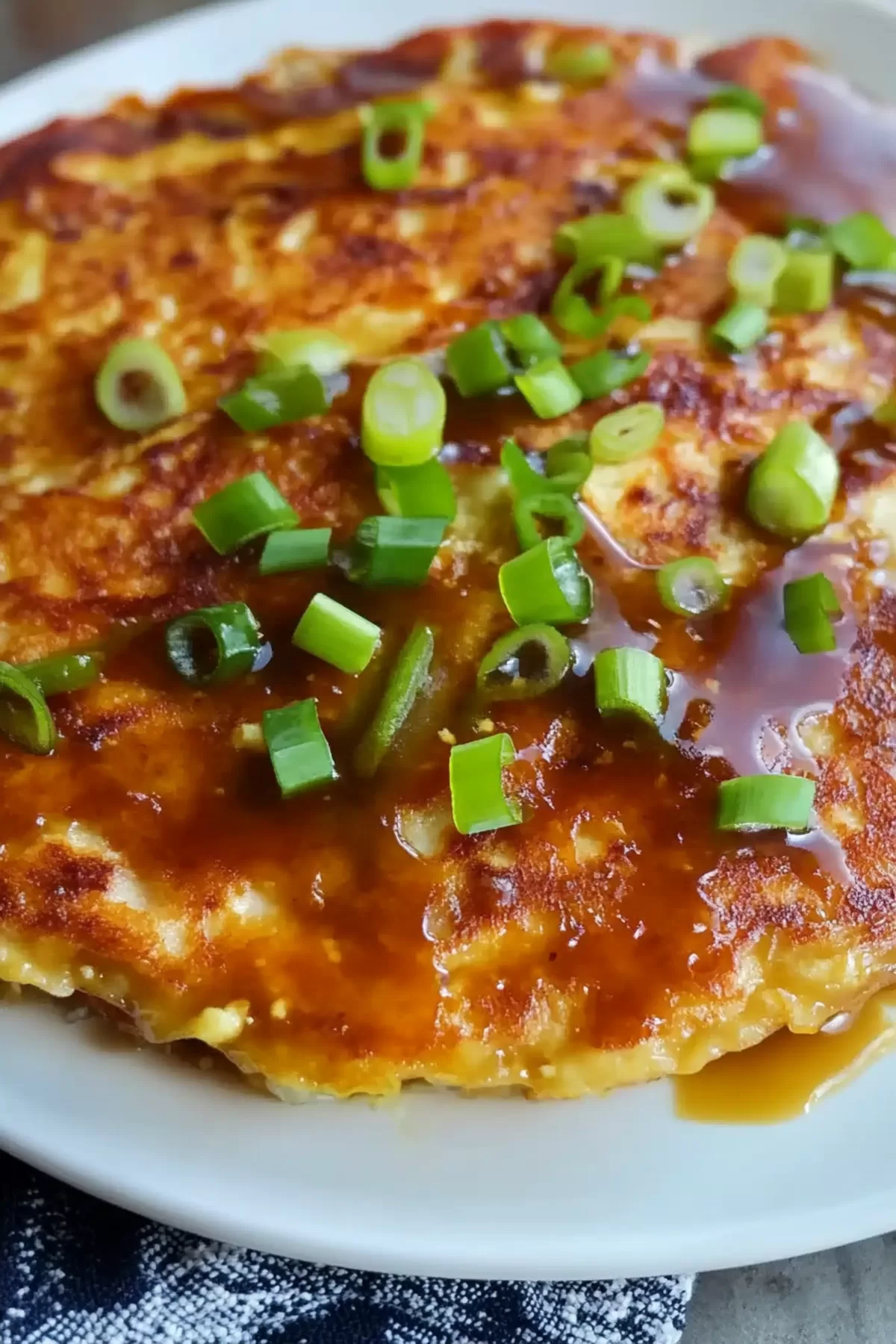 Egg Foo Young on a plate, paired with a side of dipping sauce, showcasing its caramelized surface and vibrant garnishes