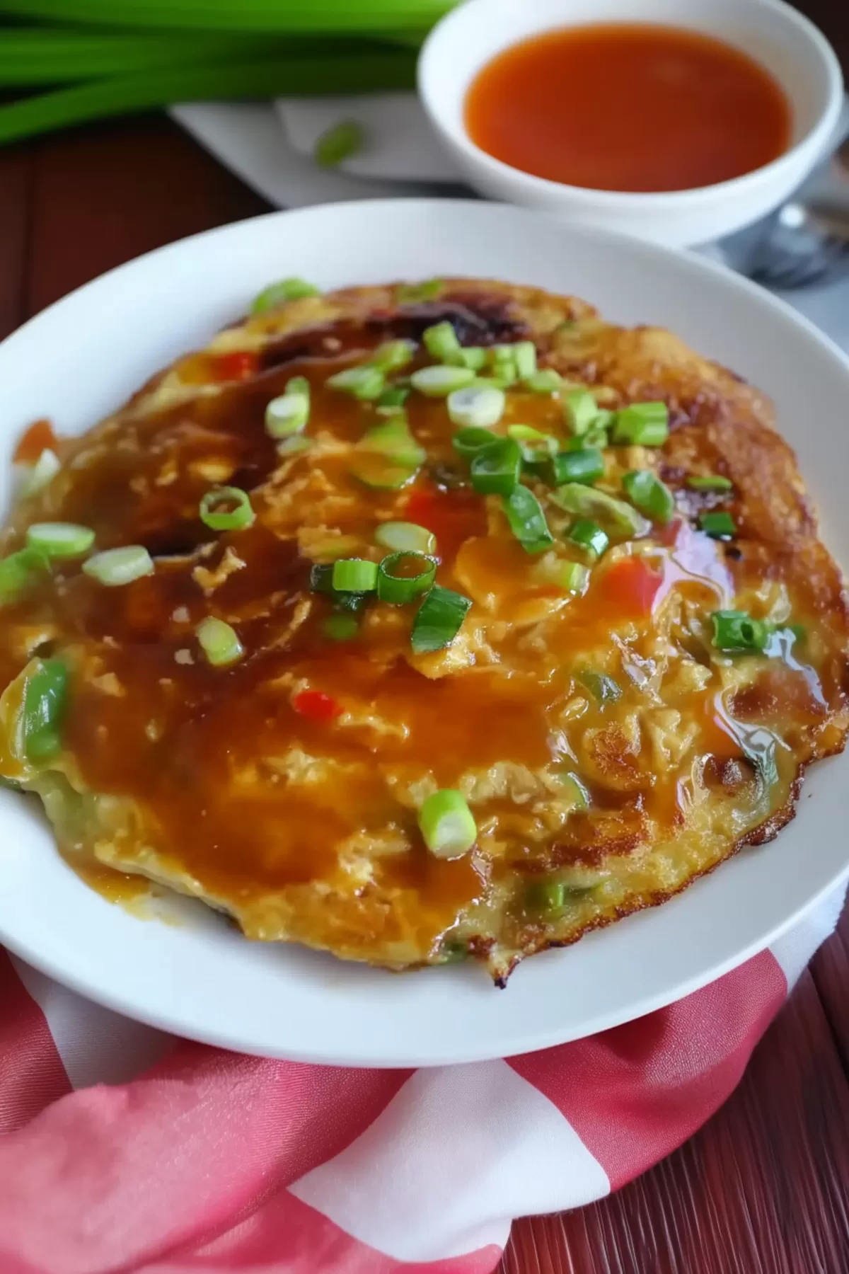 A hearty portion of Egg Foo Young garnished with chopped green onions and coated in a luscious brown gravy, highlighting its comforting appeal.