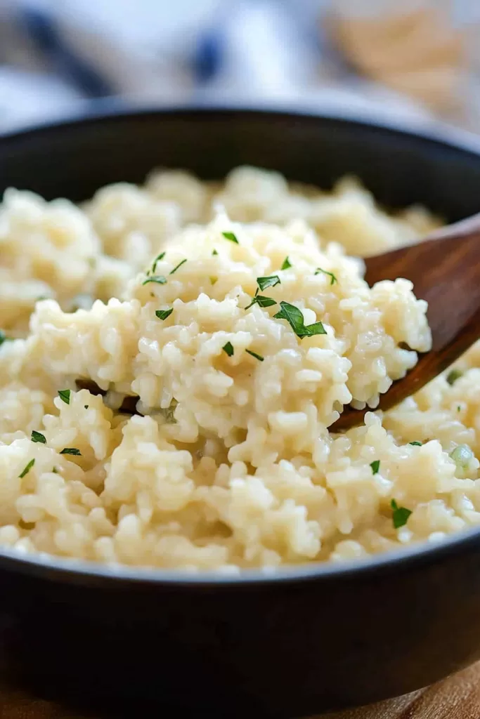 A close-up view of creamy risotto garnished with fresh parsley, served in a black bowl.