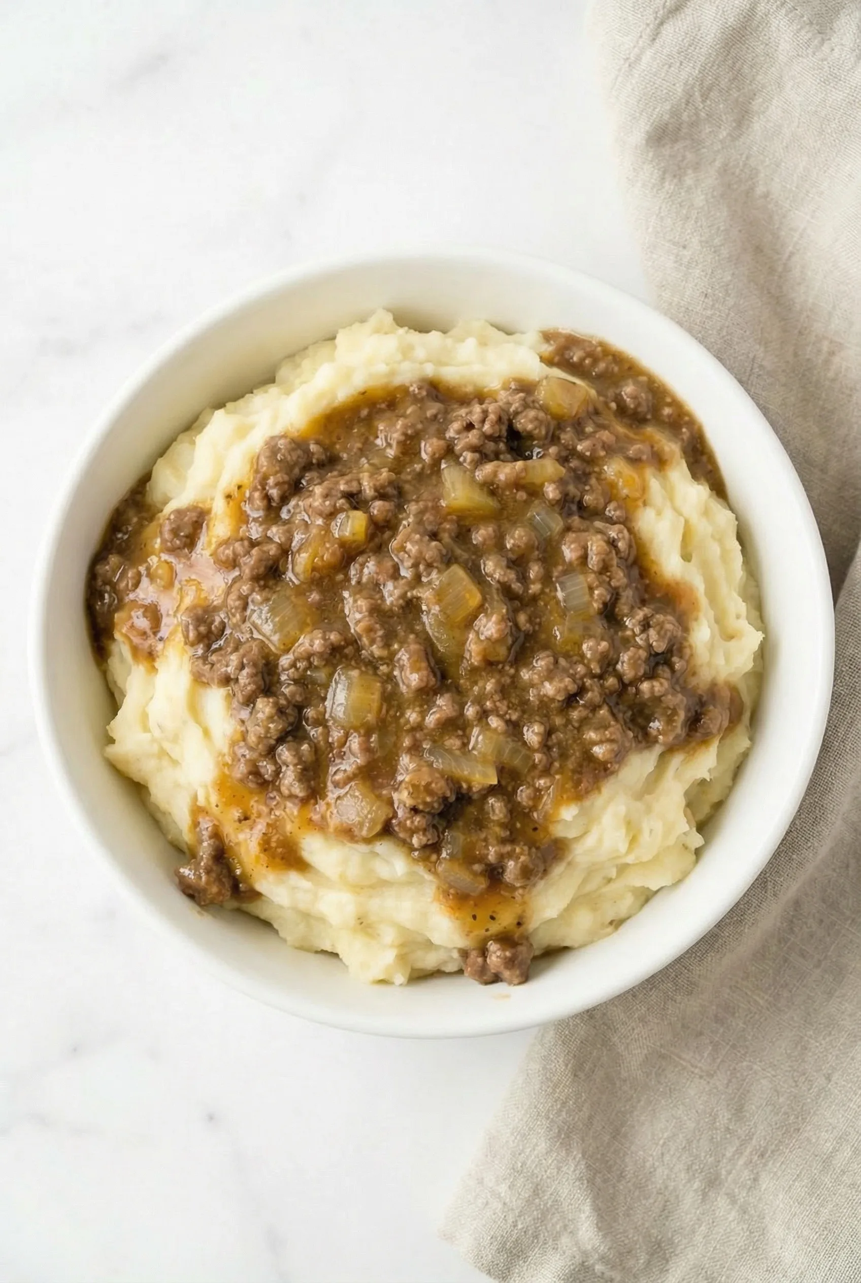 Bowl of creamy mashed potatoes topped with rich ground beef gravy and tender onions