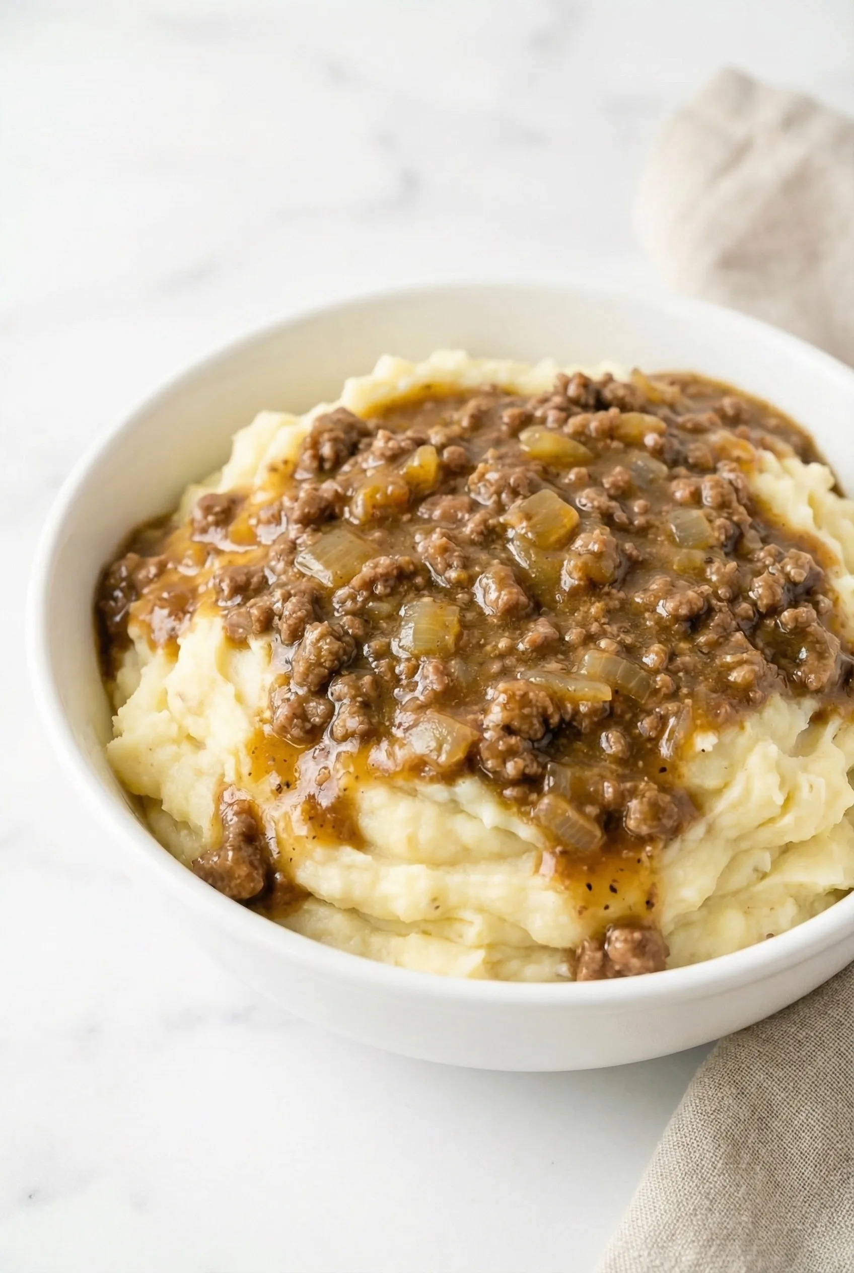 Close-up of mashed potatoes covered in savory ground beef gravy with visible onion pieces