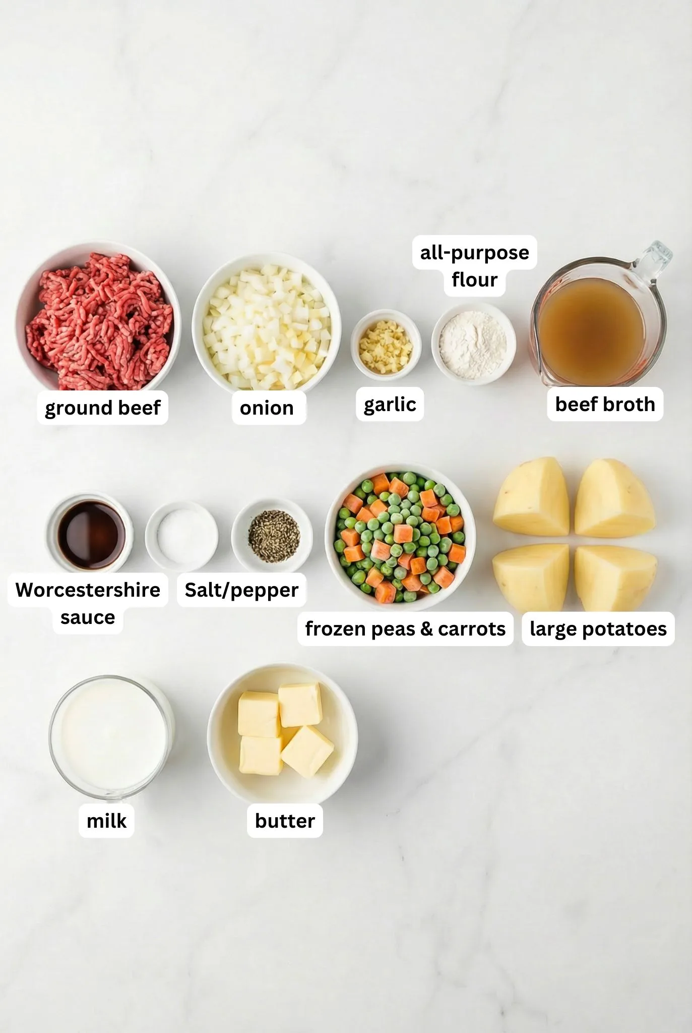 Flat lay of ground beef, potatoes, onion, garlic, flour, butter, milk, beef broth, Worcestershire sauce, and frozen peas and carrots for Ground Beef and Gravy Over Mashed Potatoes