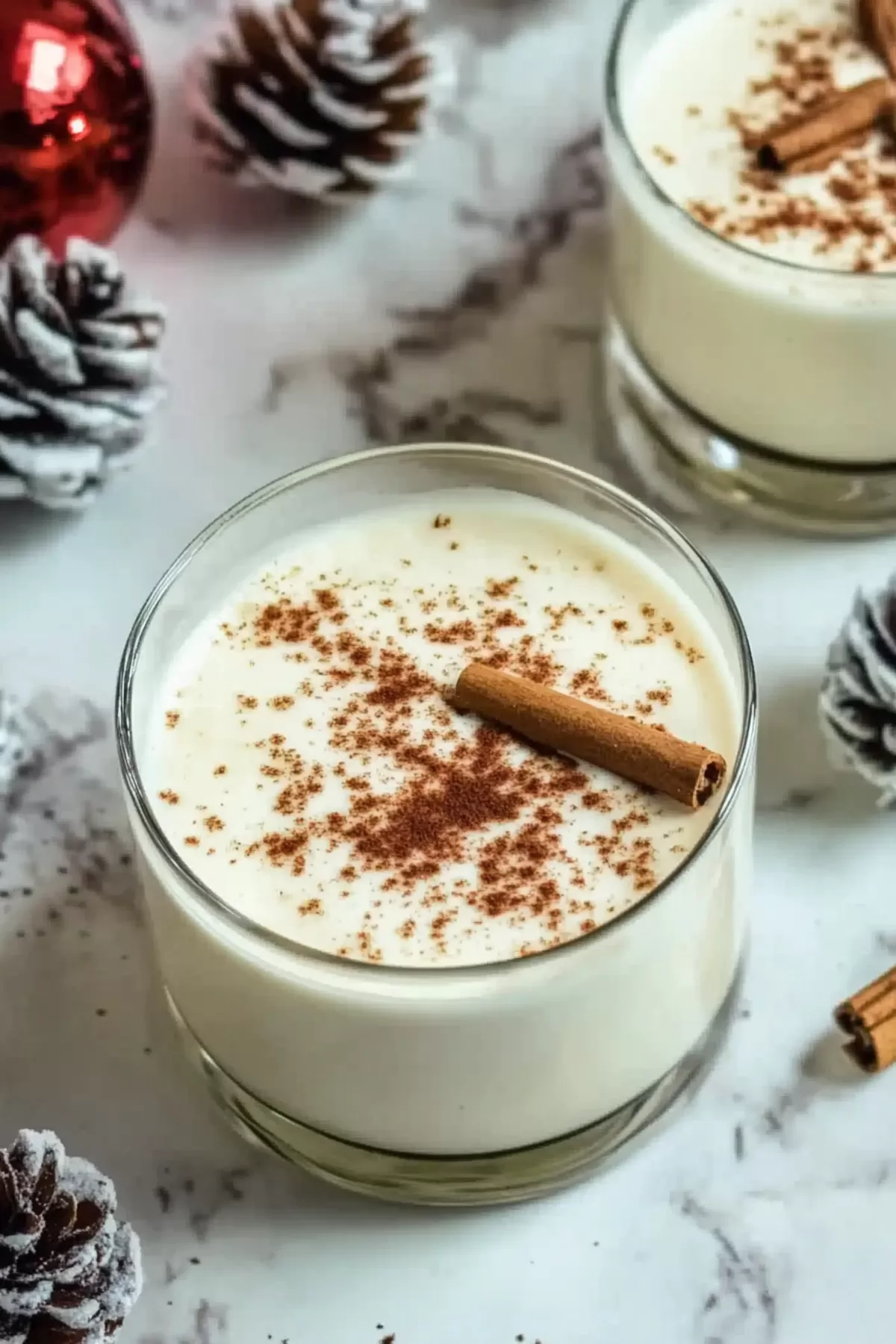 A cozy glass of homemade eggnog topped with a cinnamon stick and holiday decorations, perfect for the Christmas season.