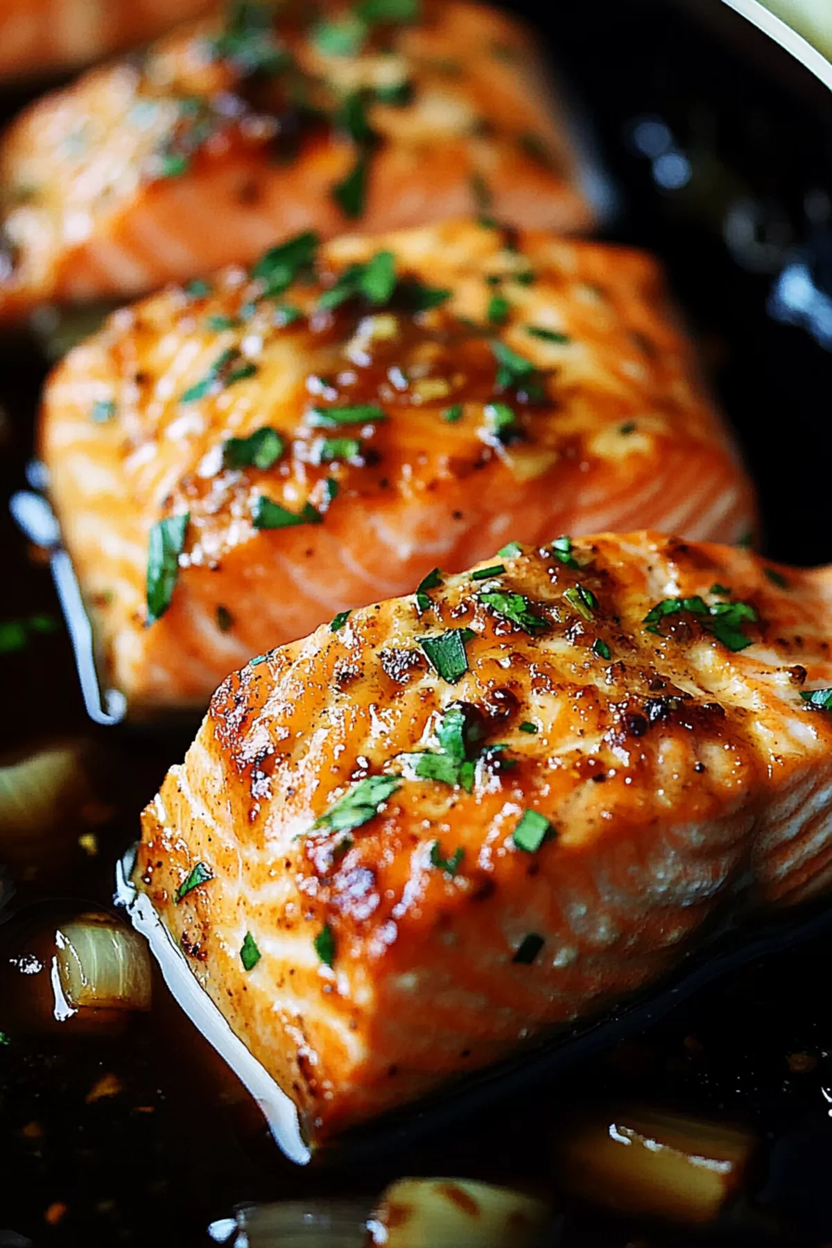 A plate of salmon topped with a glossy, caramelized honey-garlic sauce and garnished with green herbs.