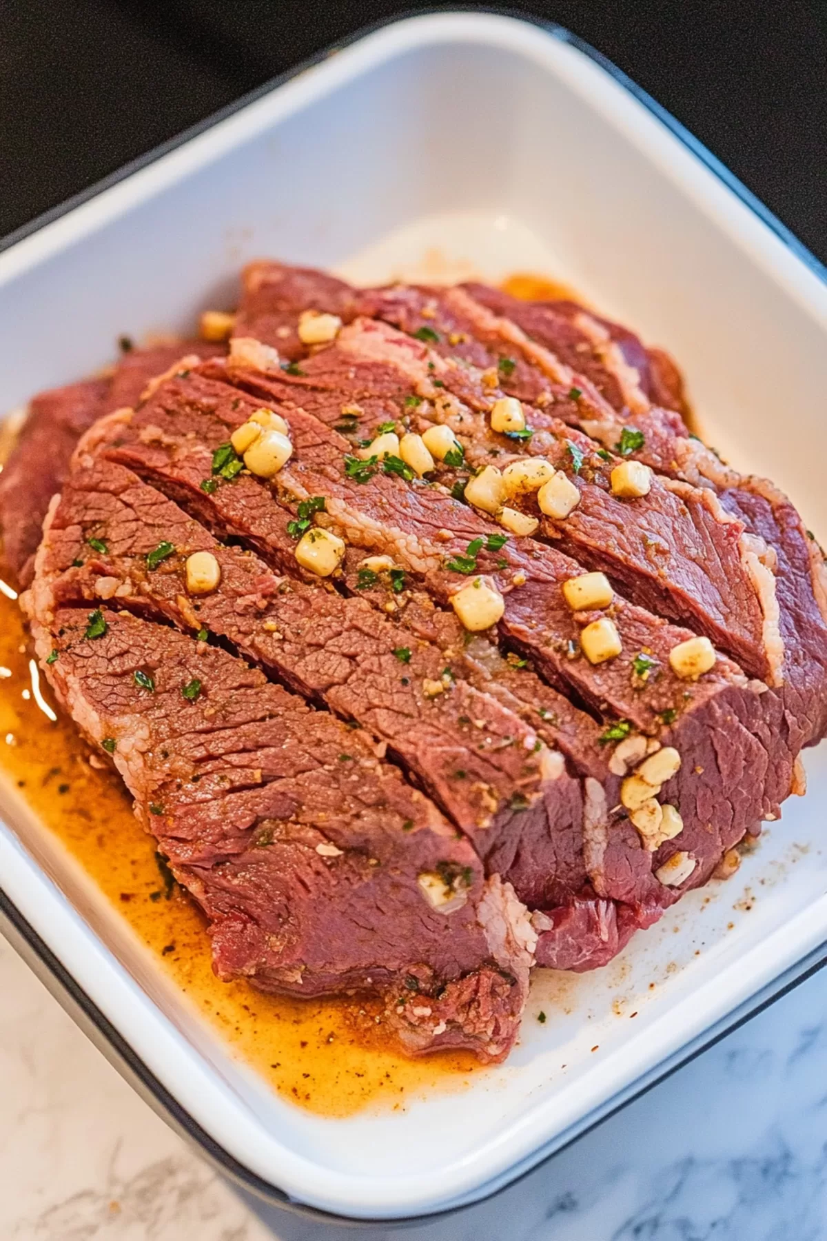 A tender corned beef brisket resting in a dish with marinade and herbs, prepped for pressure cooking.