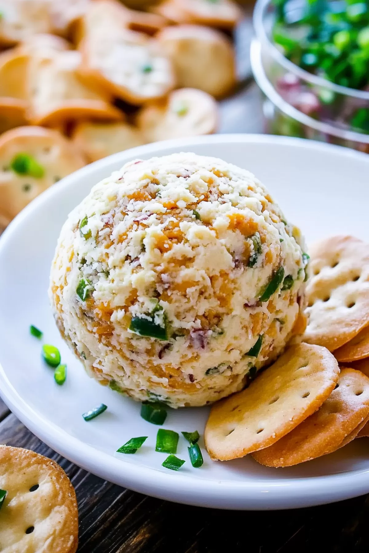 An appetizing cheese ball garnished with sharp cheddar, jalapeños, and bacon, sitting in a white bowl surrounded by buttery crackers.