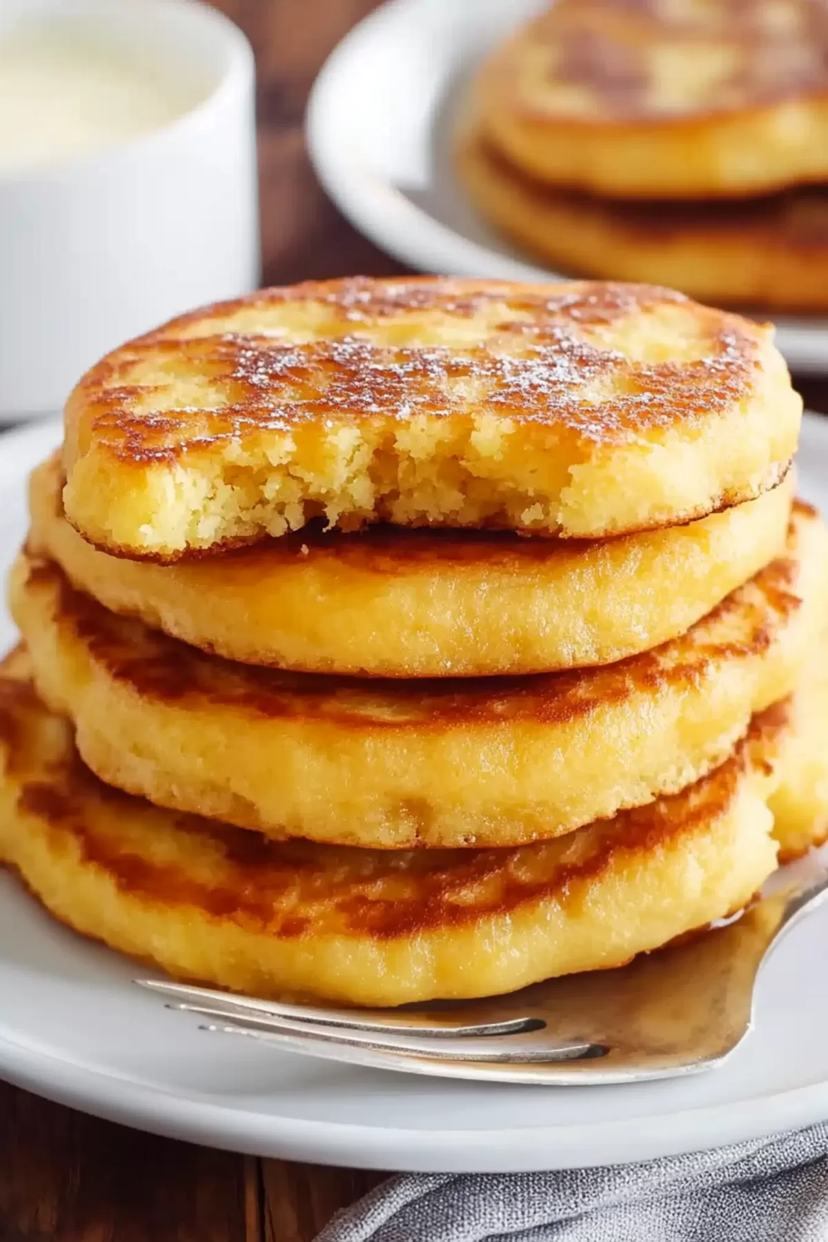 A stack of pancakes with a bite taken out of the top one, revealing a soft, tender crumb.