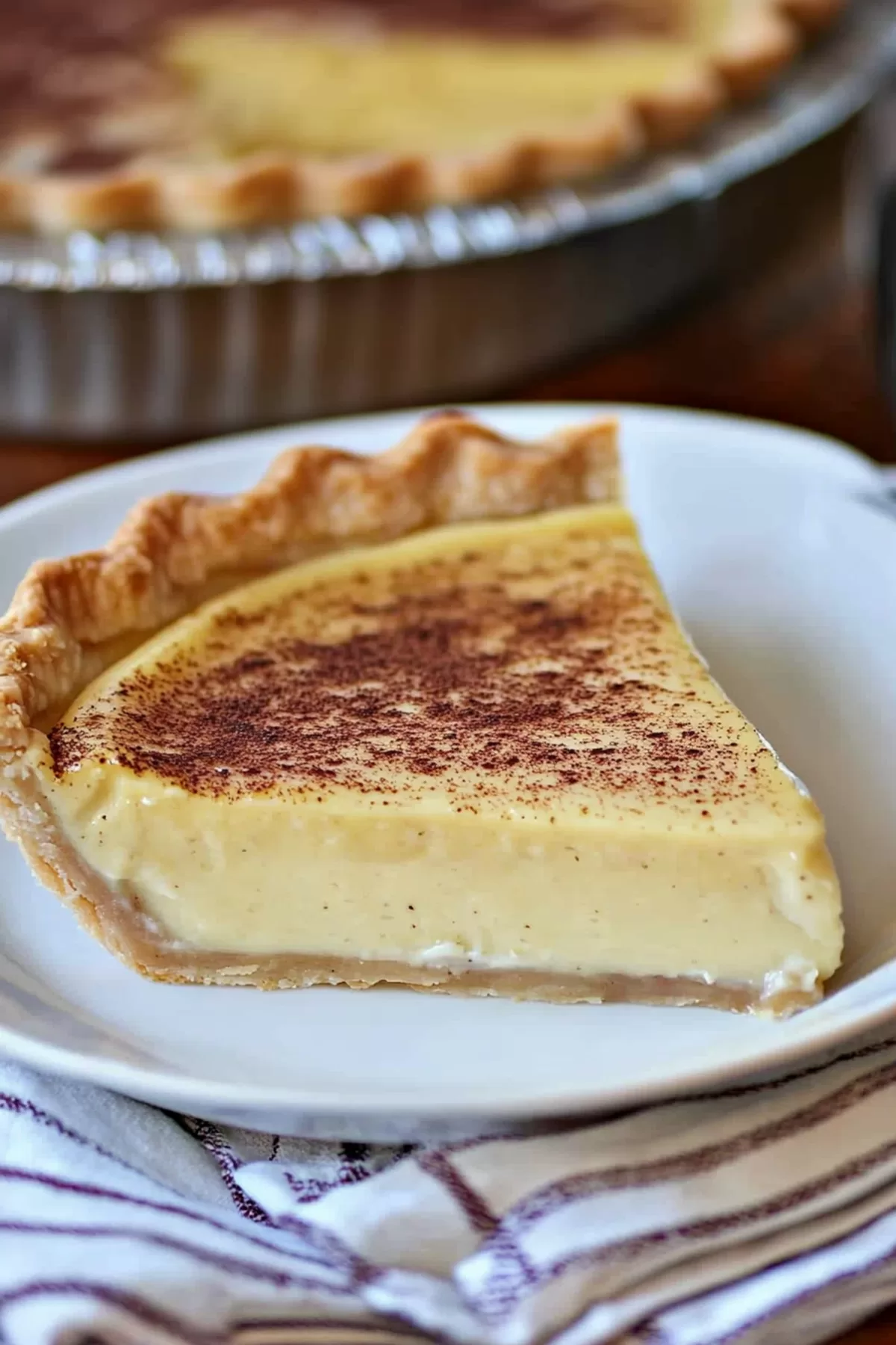 A slice of golden, creamy pie with a dusting of nutmeg, sitting on a white plate.