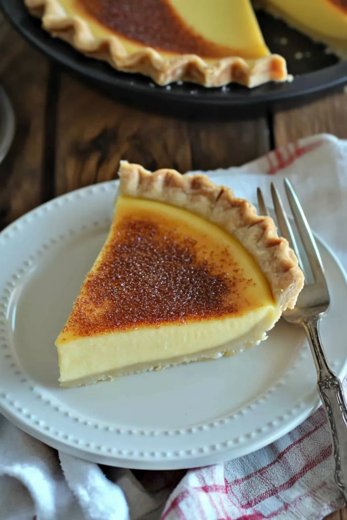 A rich custard pie slice, served with a fork on a decorative plate.