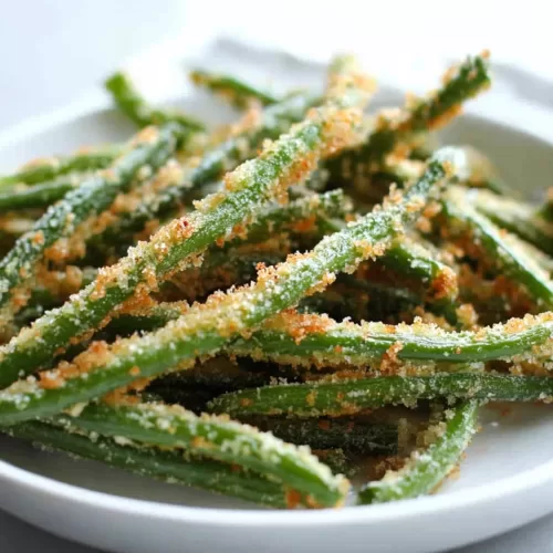 Crispy green bean fries with a golden breadcrumb coating served in a white plate, perfect for snacking.