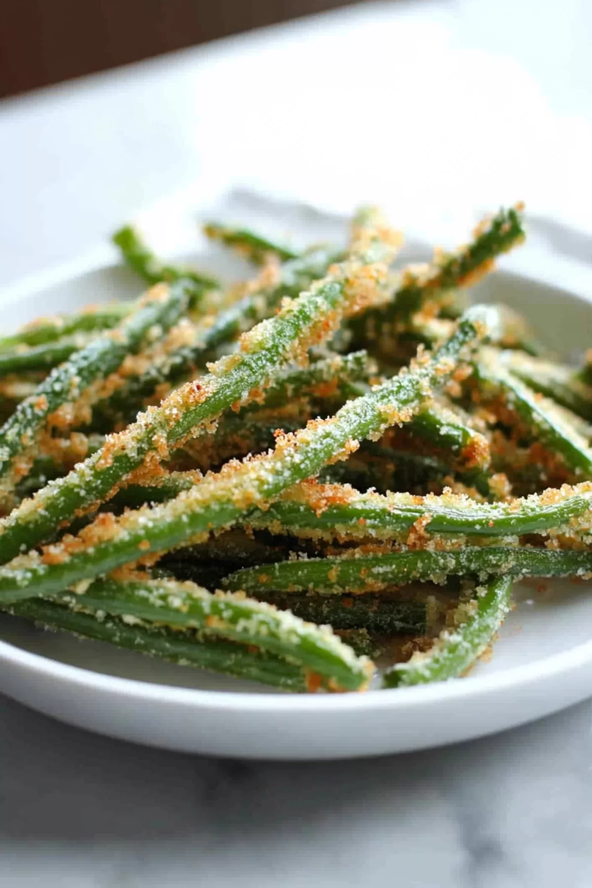 Crispy green bean fries with a golden breadcrumb coating served in a white plate, perfect for snacking.