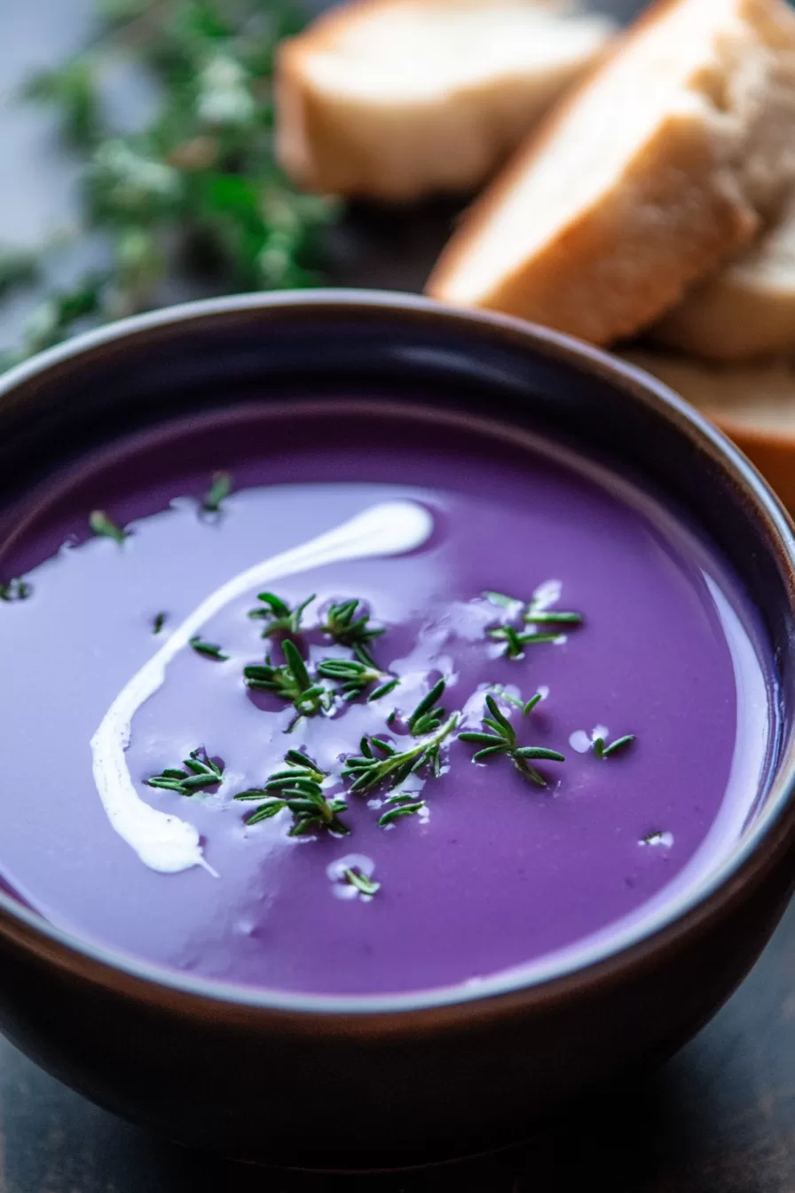 A healthy and vibrant soup in a white bowl, highlighting its deep purple color and fresh garnish.