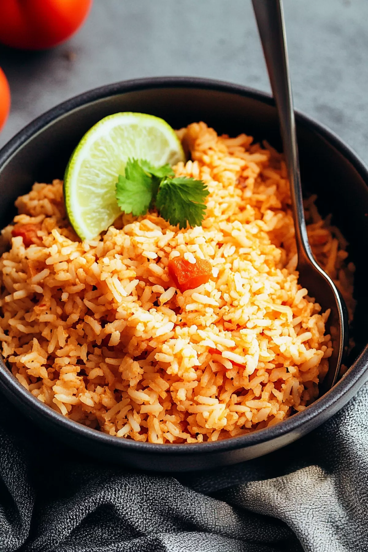 A bowl of fluffy rice with a rich reddish hue, garnished with fresh cilantro and lime wedges.