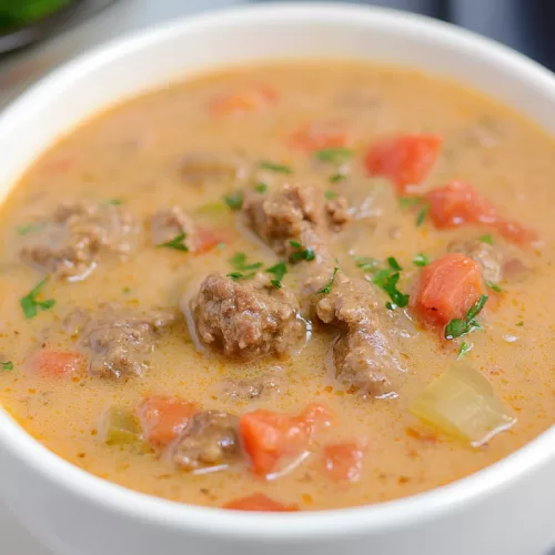 Close-up of a steaming bowl of rich, cheesy soup with ground beef and potatoes.