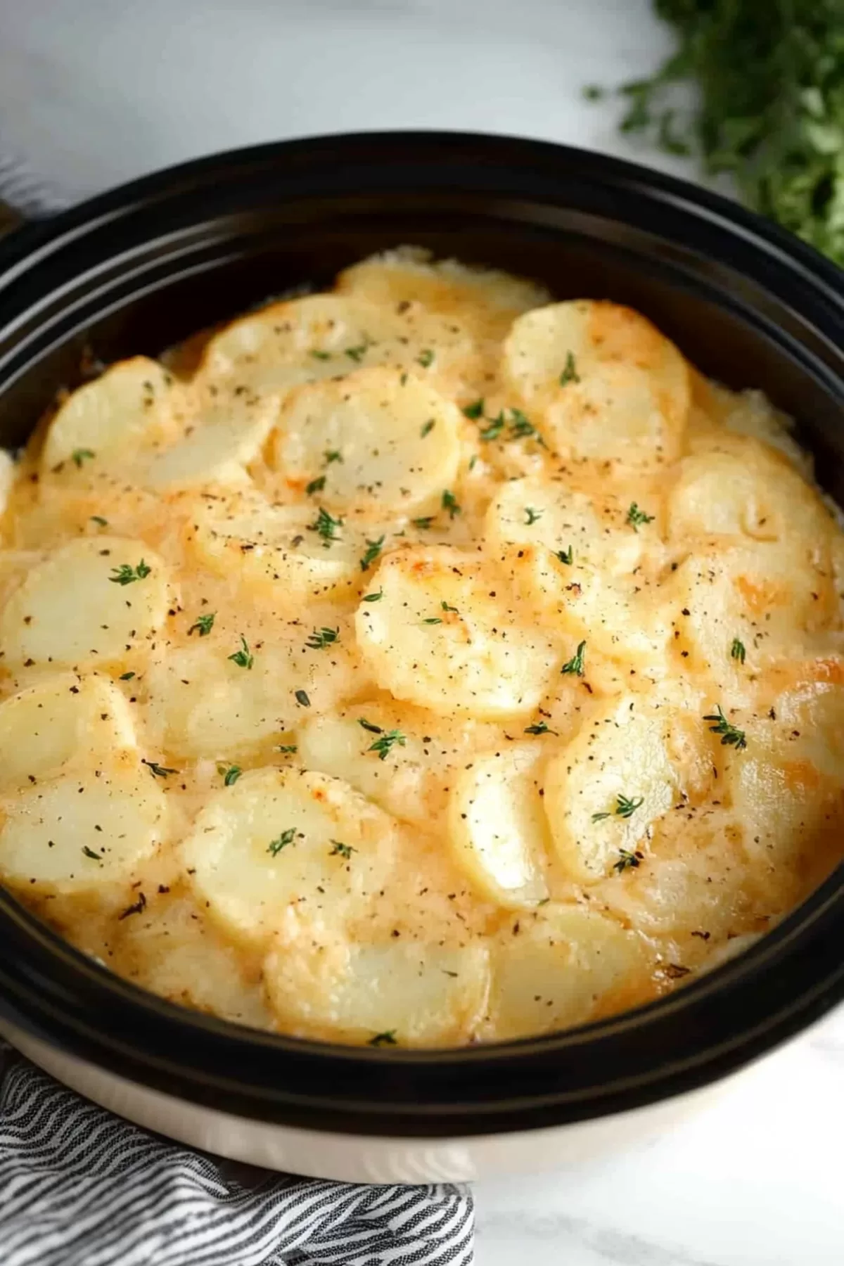 Potatoes layered in a slow cooker with bubbling cheese and crispy edges.