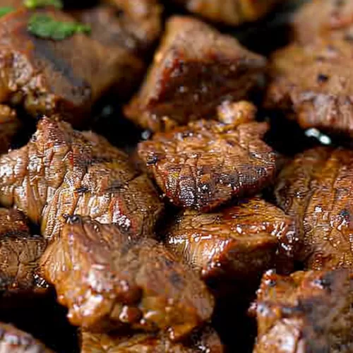 Overhead view of steak pieces coated in a Cajun-spiced butter sauce, creating a rich, glossy finish.