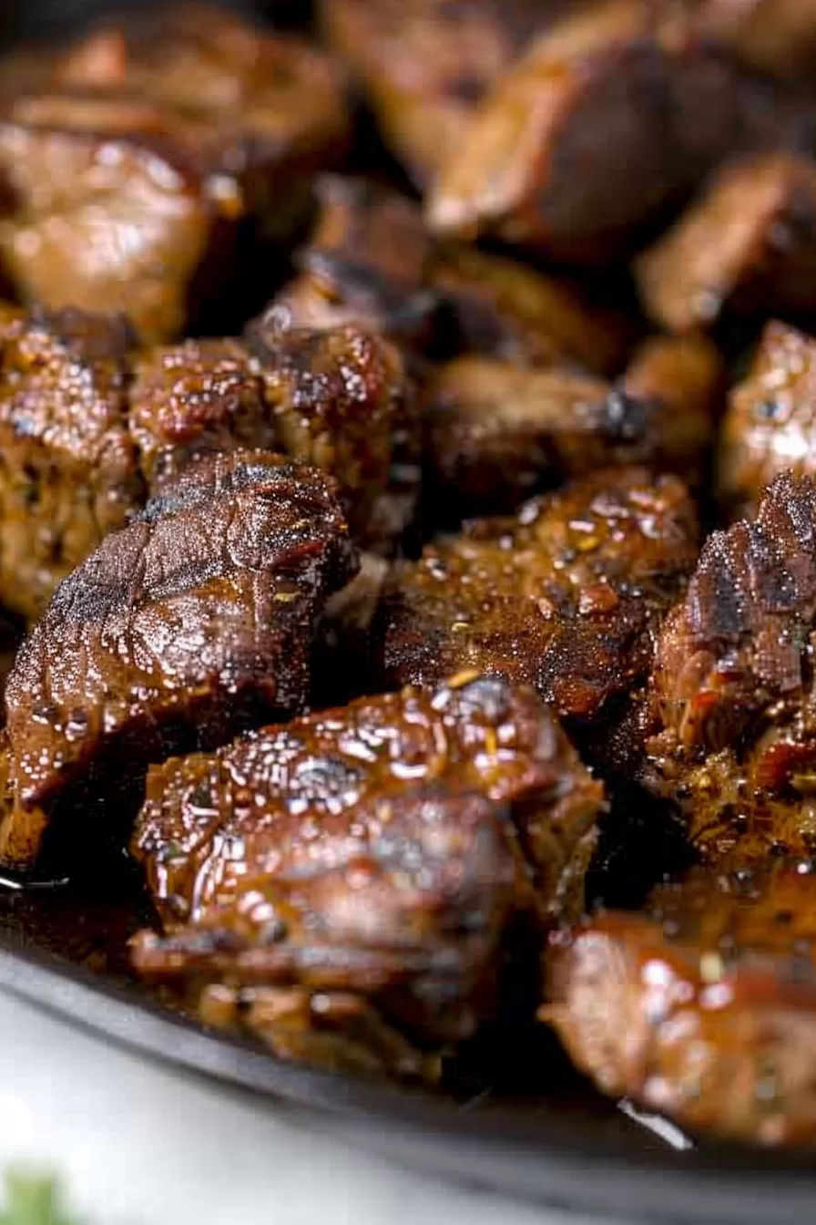 Close-up of perfectly seared steak bites with a rich, golden glaze, garnished with fresh herbs.