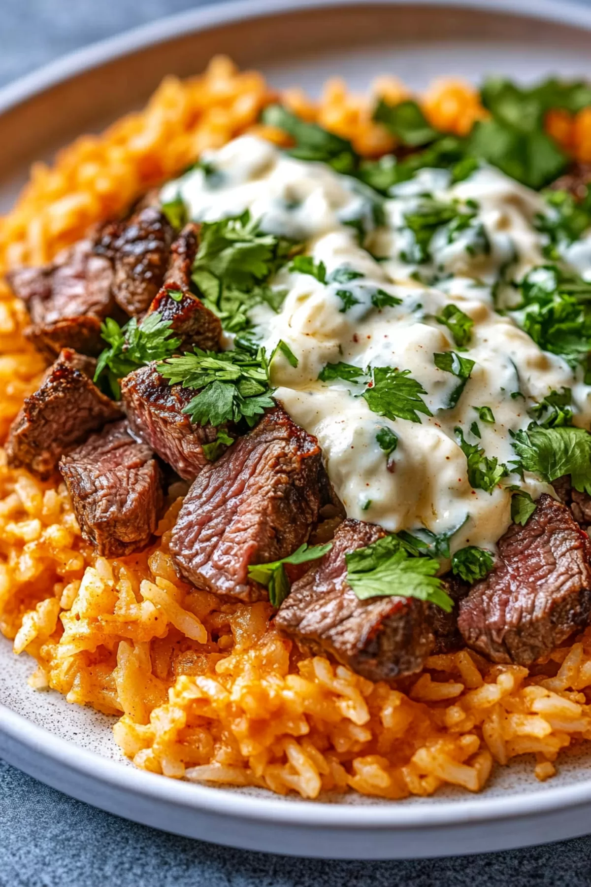 A close-up of steak pieces resting on a bed of seasoned rice, garnished with fresh herbs.