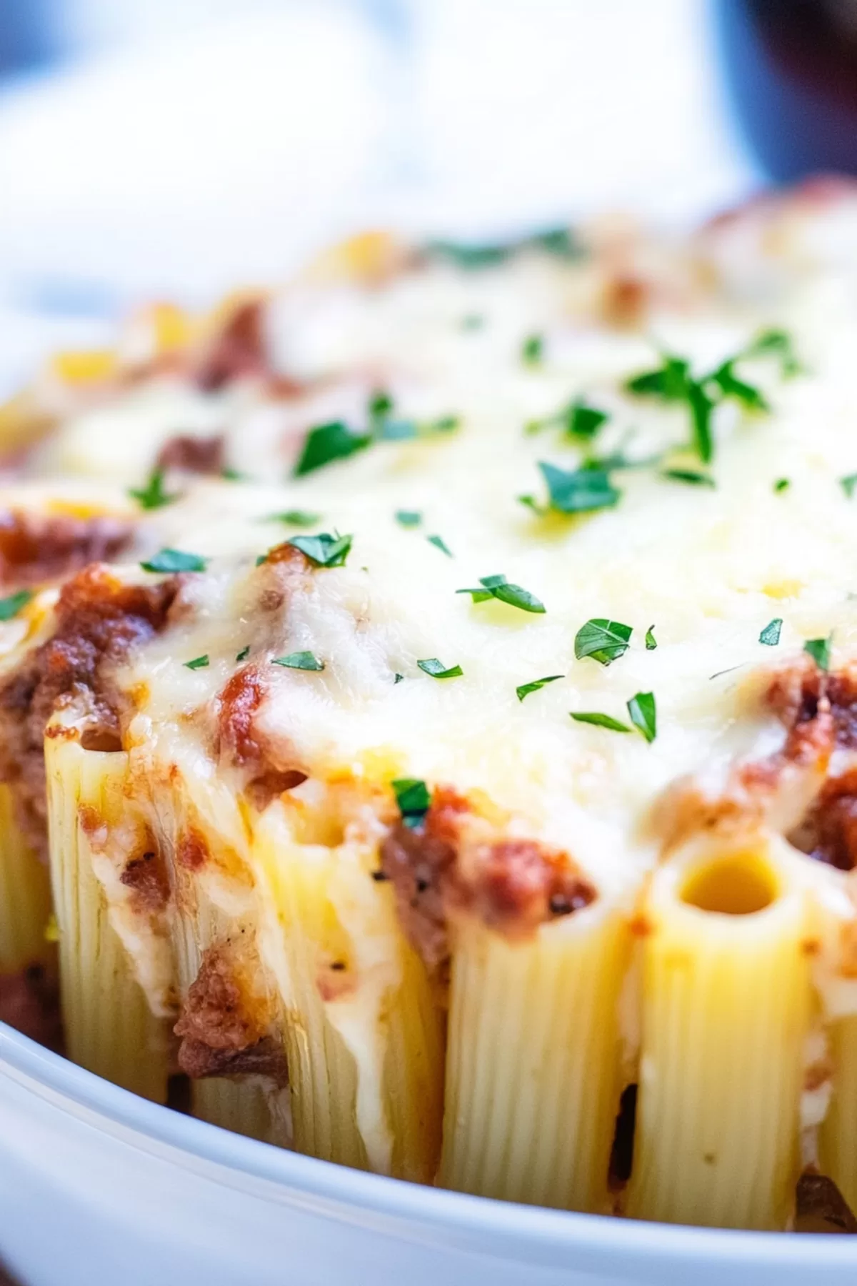 A casserole dish filled with layered rigatoni topped with melted cheese and fresh herbs.