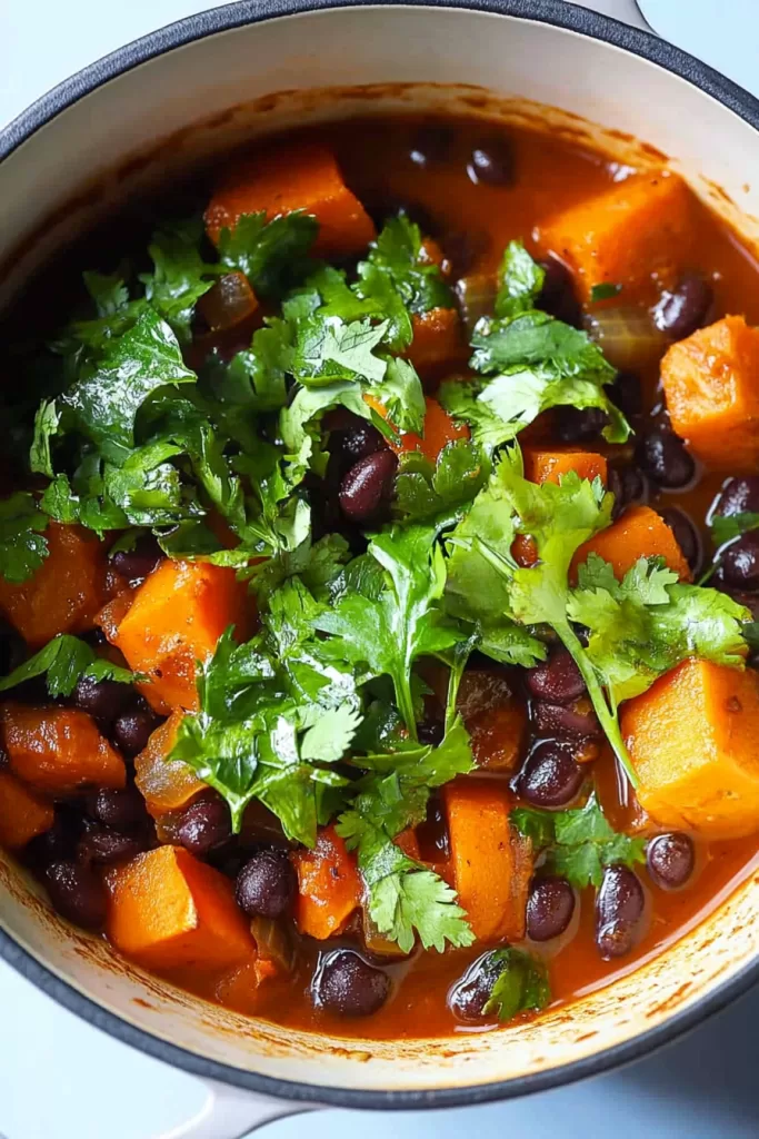 Close-up of a vibrant stew with tender sweet potato chunks, black beans, and a garnish of fresh cilantro in a rustic pot.