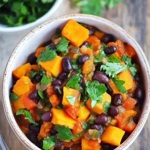 Bowl of hearty soup featuring diced sweet potatoes, black beans, and a sprinkle of fresh herbs, served on a wooden table.