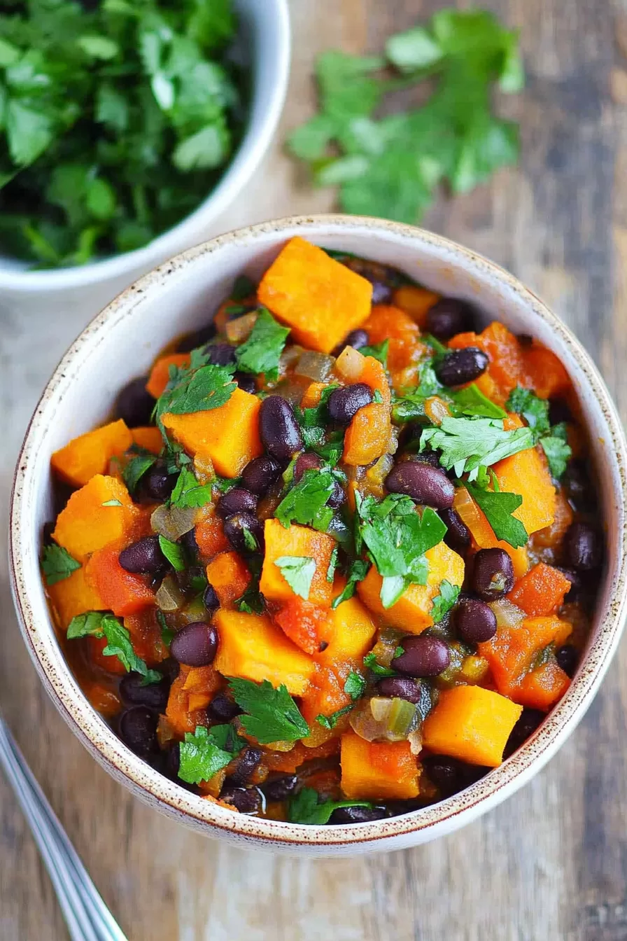 Bowl of hearty soup featuring diced sweet potatoes, black beans, and a sprinkle of fresh herbs, served on a wooden table.